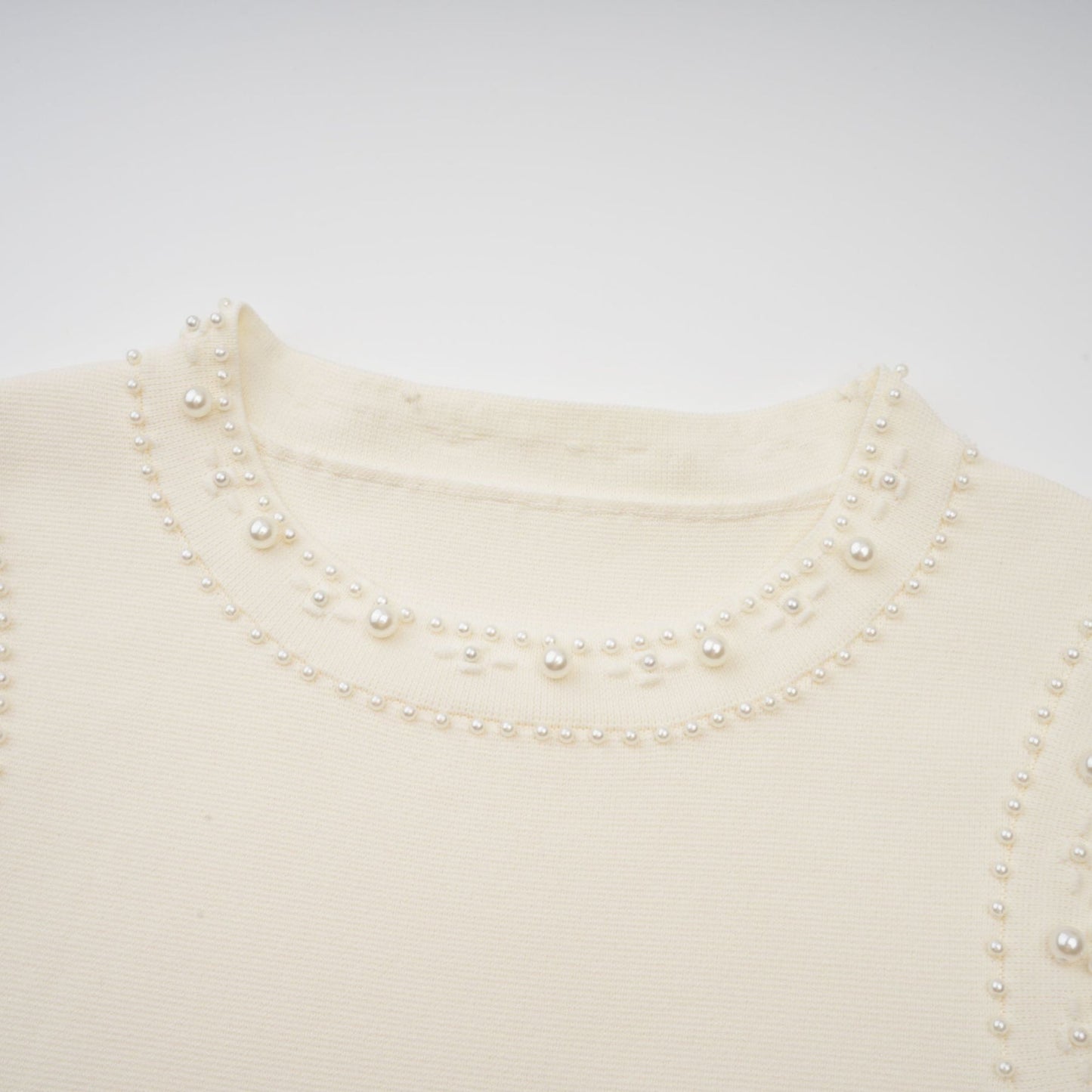 A long white knitted maxi dress with faux pearl embellishments throughout the fabric