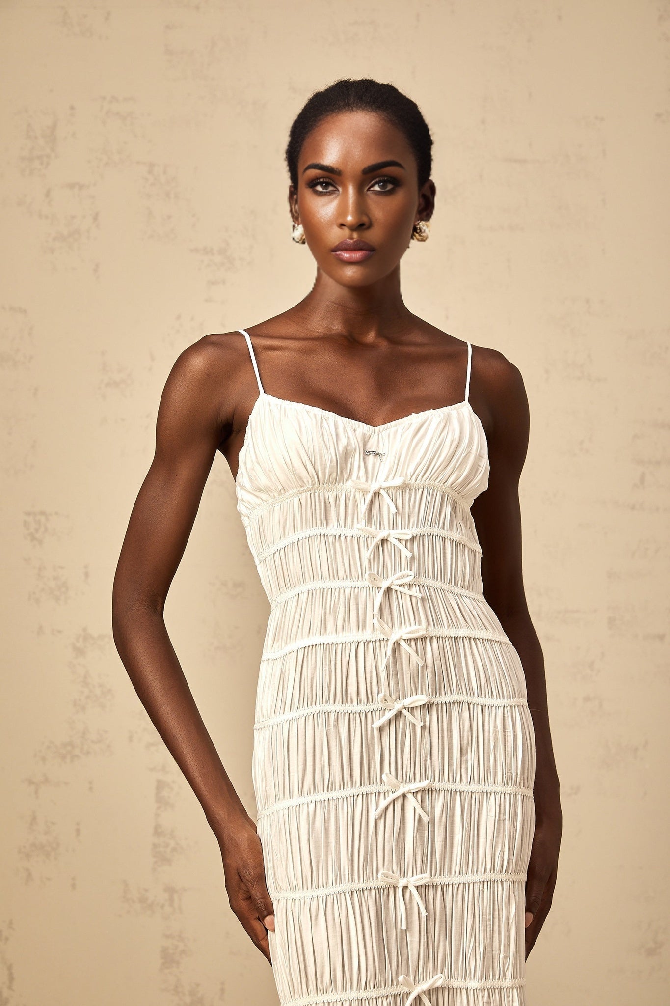 A long white maxi dress with a smocked bodice and a decorative bowknot detail