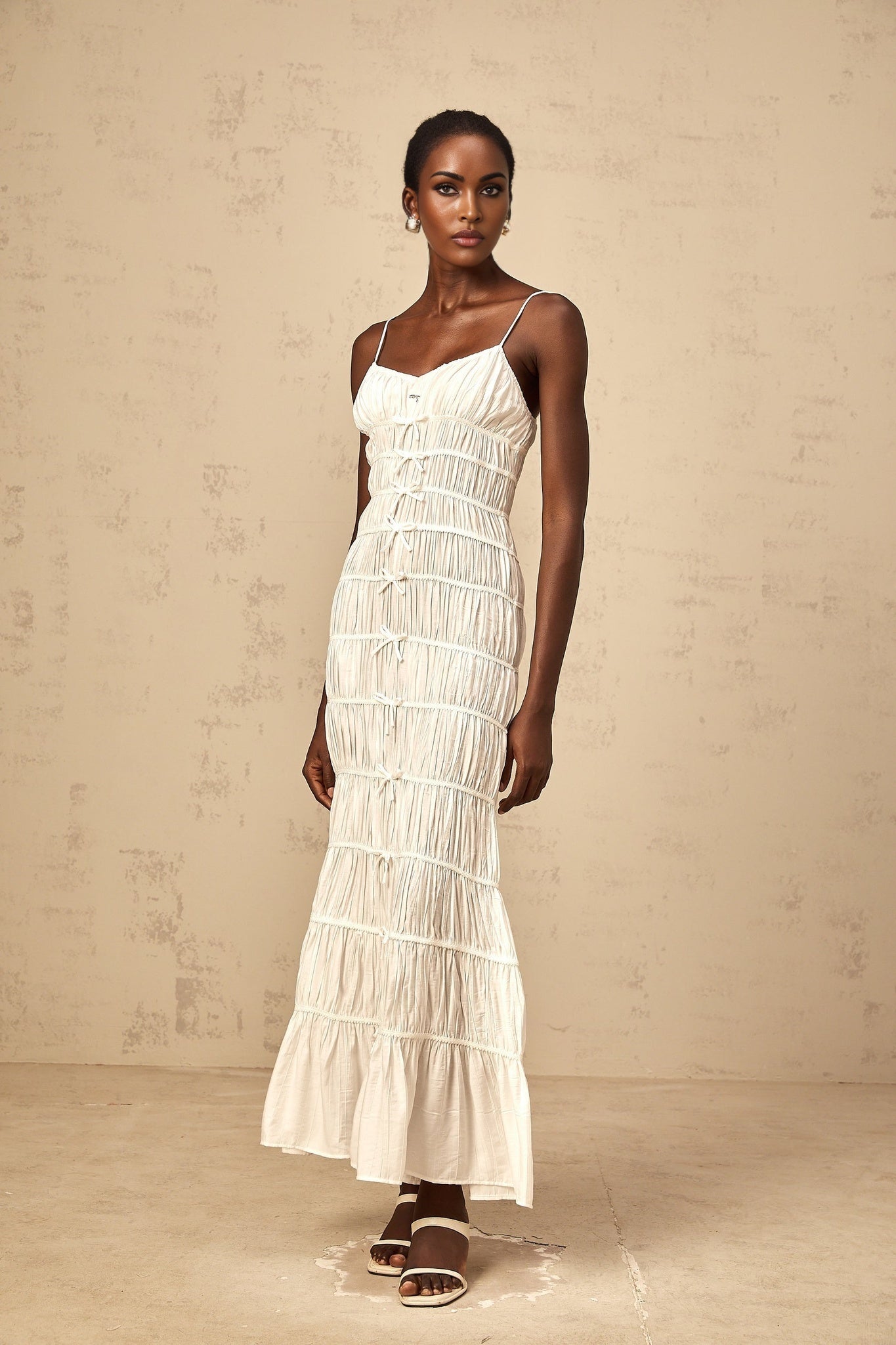 A long white maxi dress with a smocked bodice and a large bow accent at the neckline