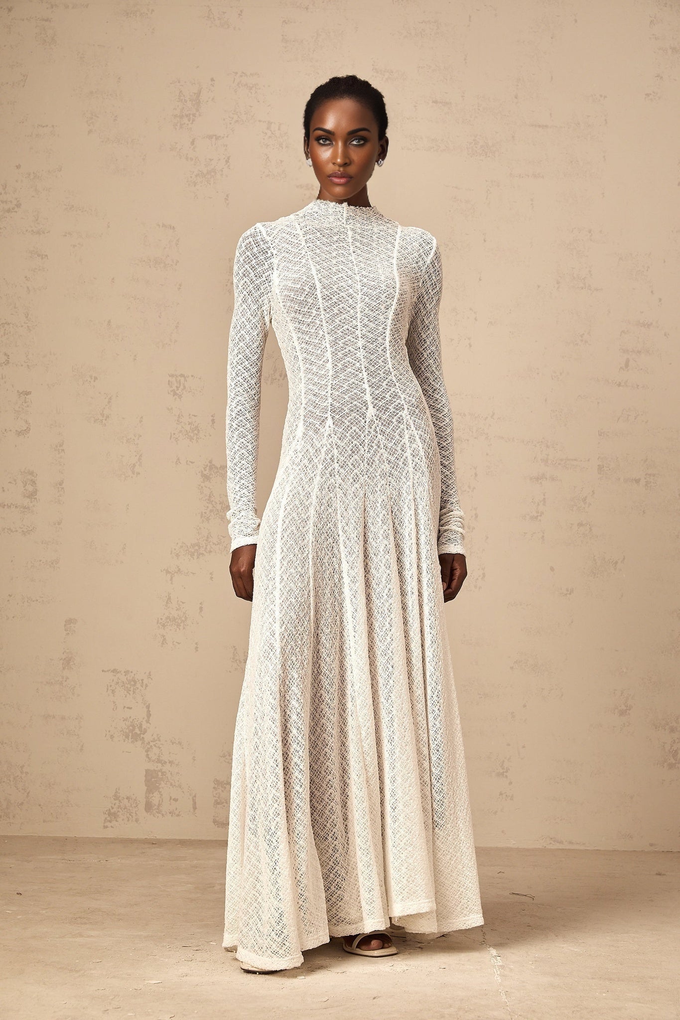 A long white maxi dress with a wavy lace pattern covering the entire garment featuring a feminine and elegant design