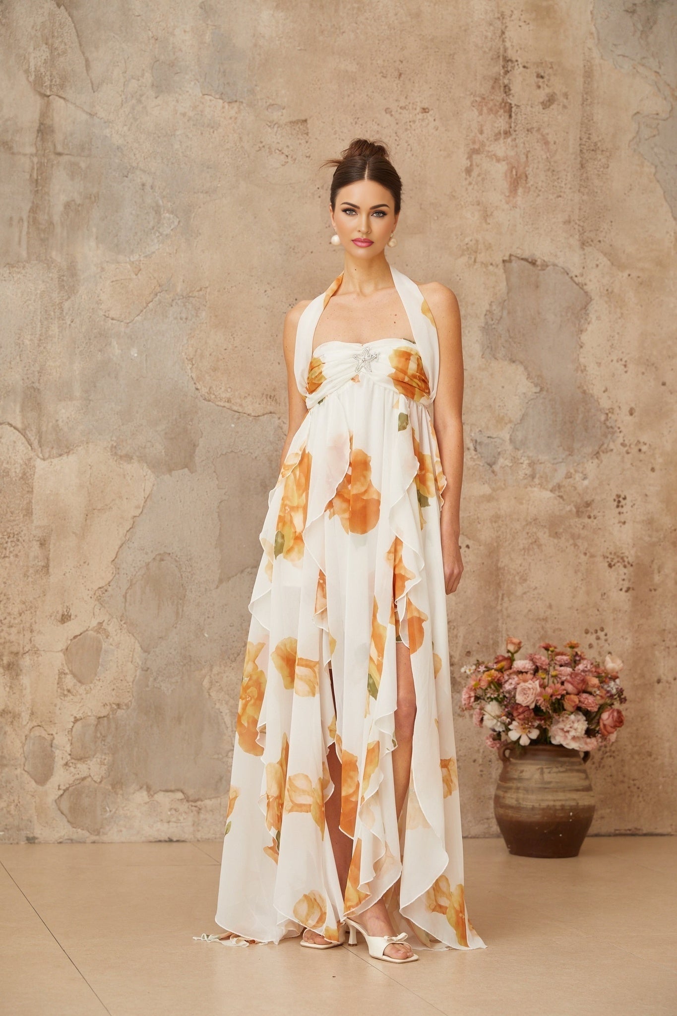 A long white maxi dress with floral print and ruffled tulle details modeled on a woman against a plain background