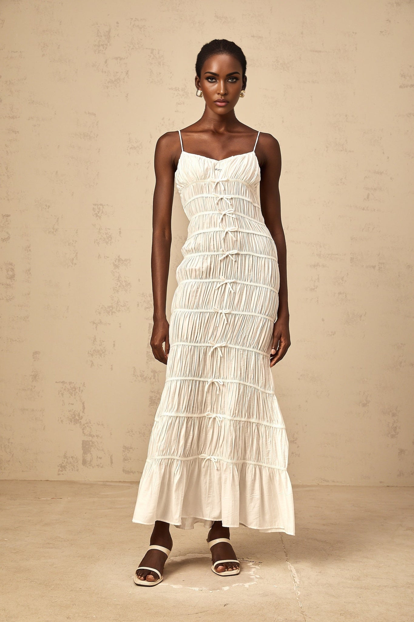 A long white maxi dress with smocked detailing and a decorative bowknot accent