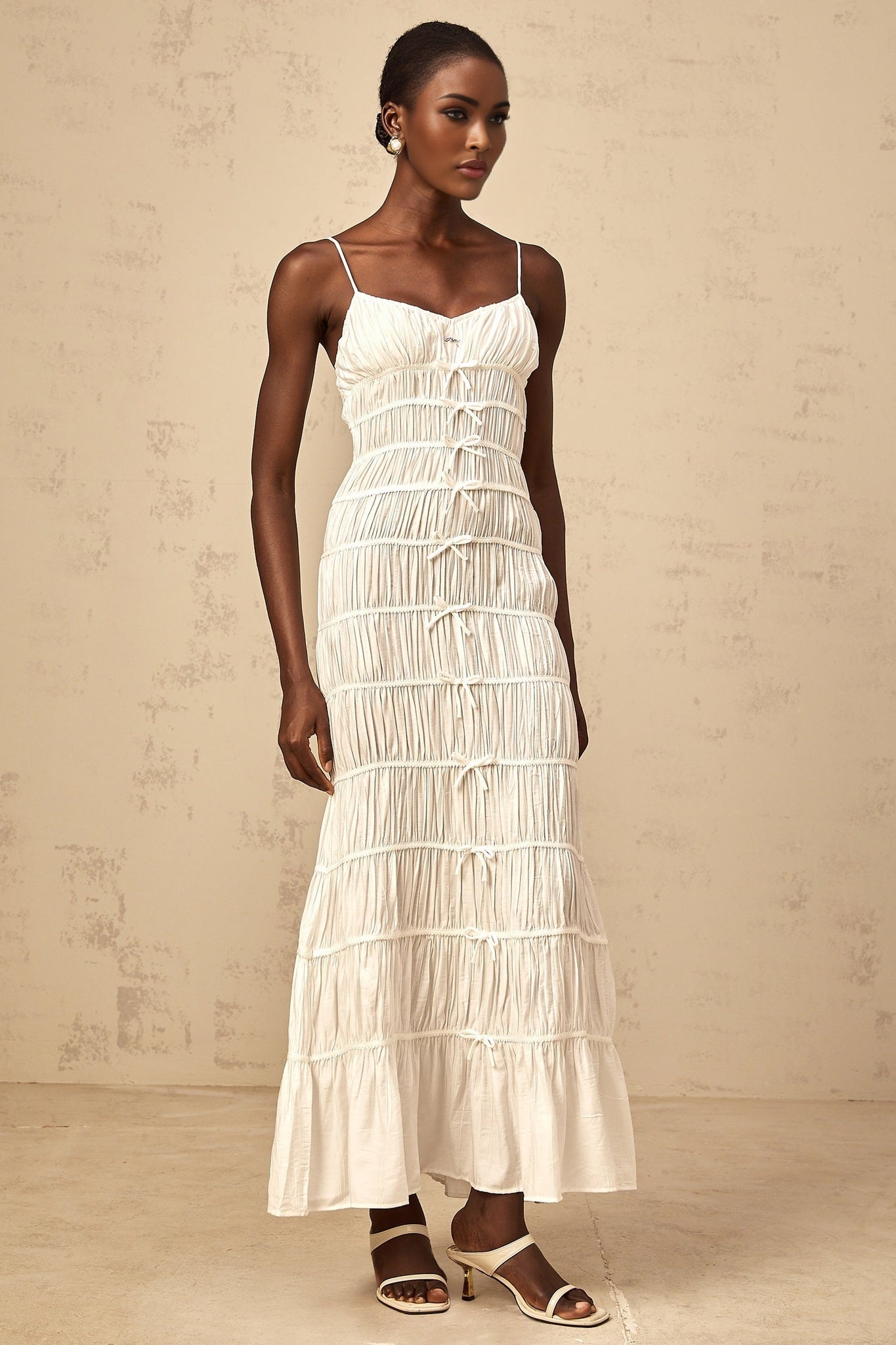 A long white maxi dress with smocked detailing and a large bow accent at the neckline