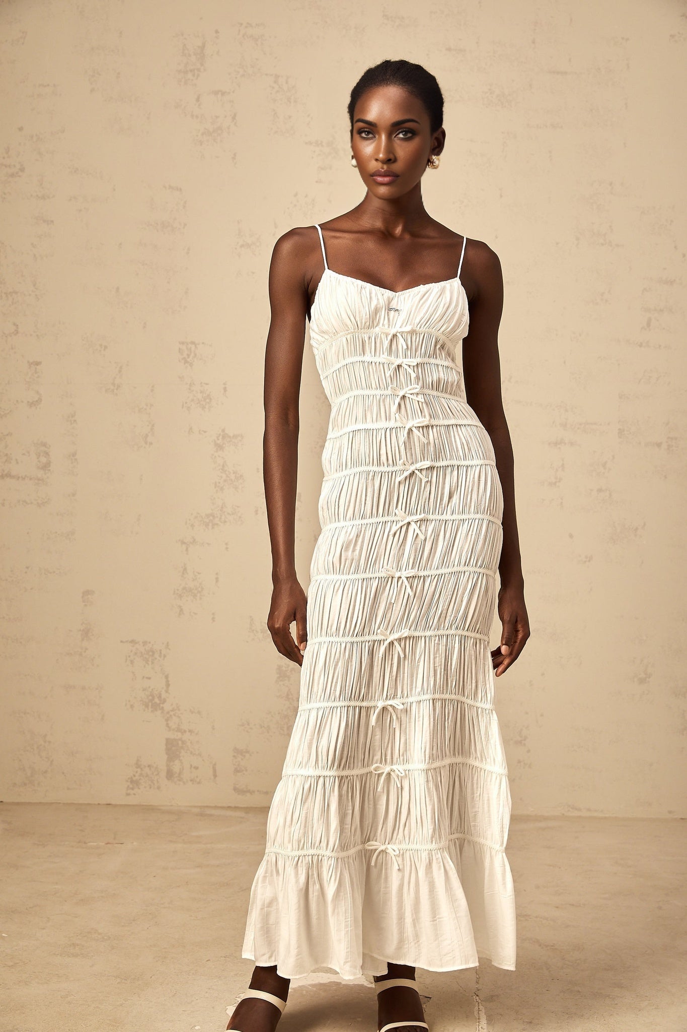 A long white maxi dress with smocked detailing and a large bow accent at the neckline