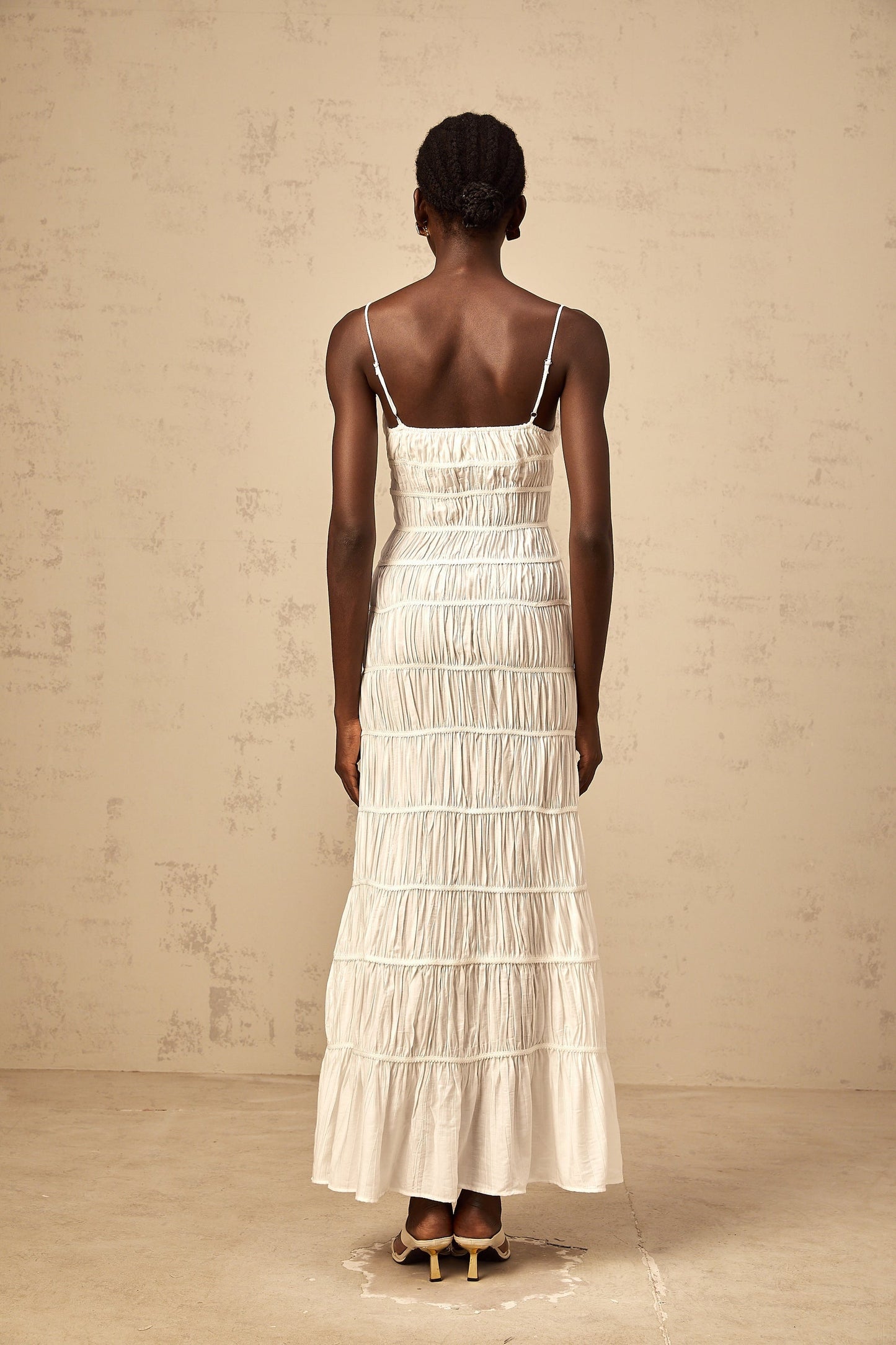 A long white maxi dress with smocked detailing and a large bow accent at the neckline
