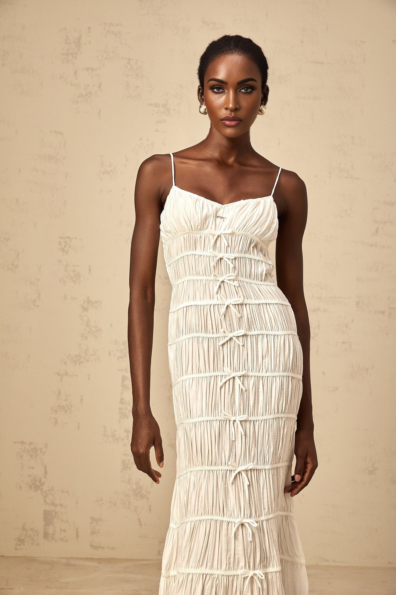 A long white maxi dress with smocked detailing and a large bow accent at the neckline