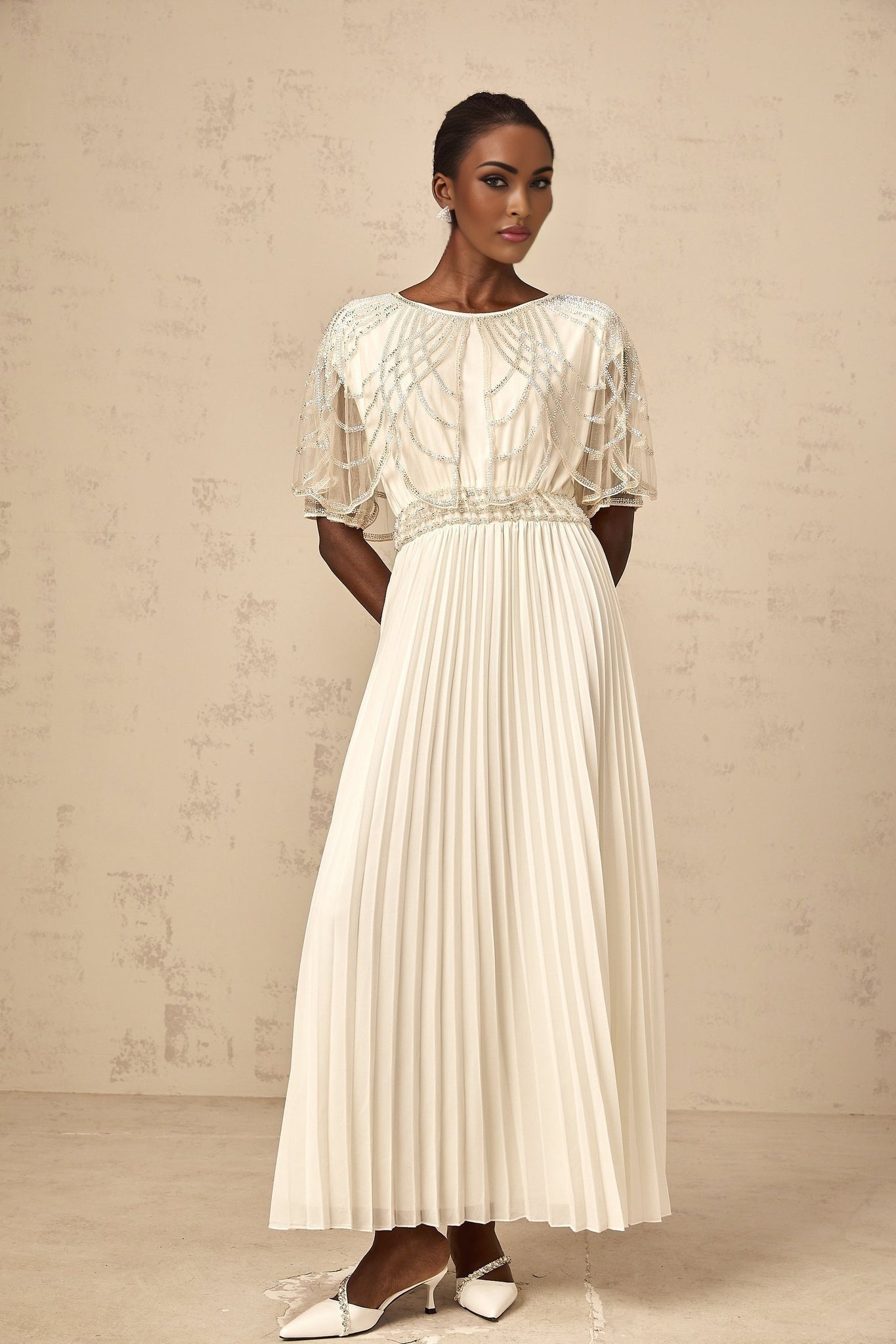 A long white pleated maxi dress adorned with crystal embellishments featuring a flowy silhouette and elegant design