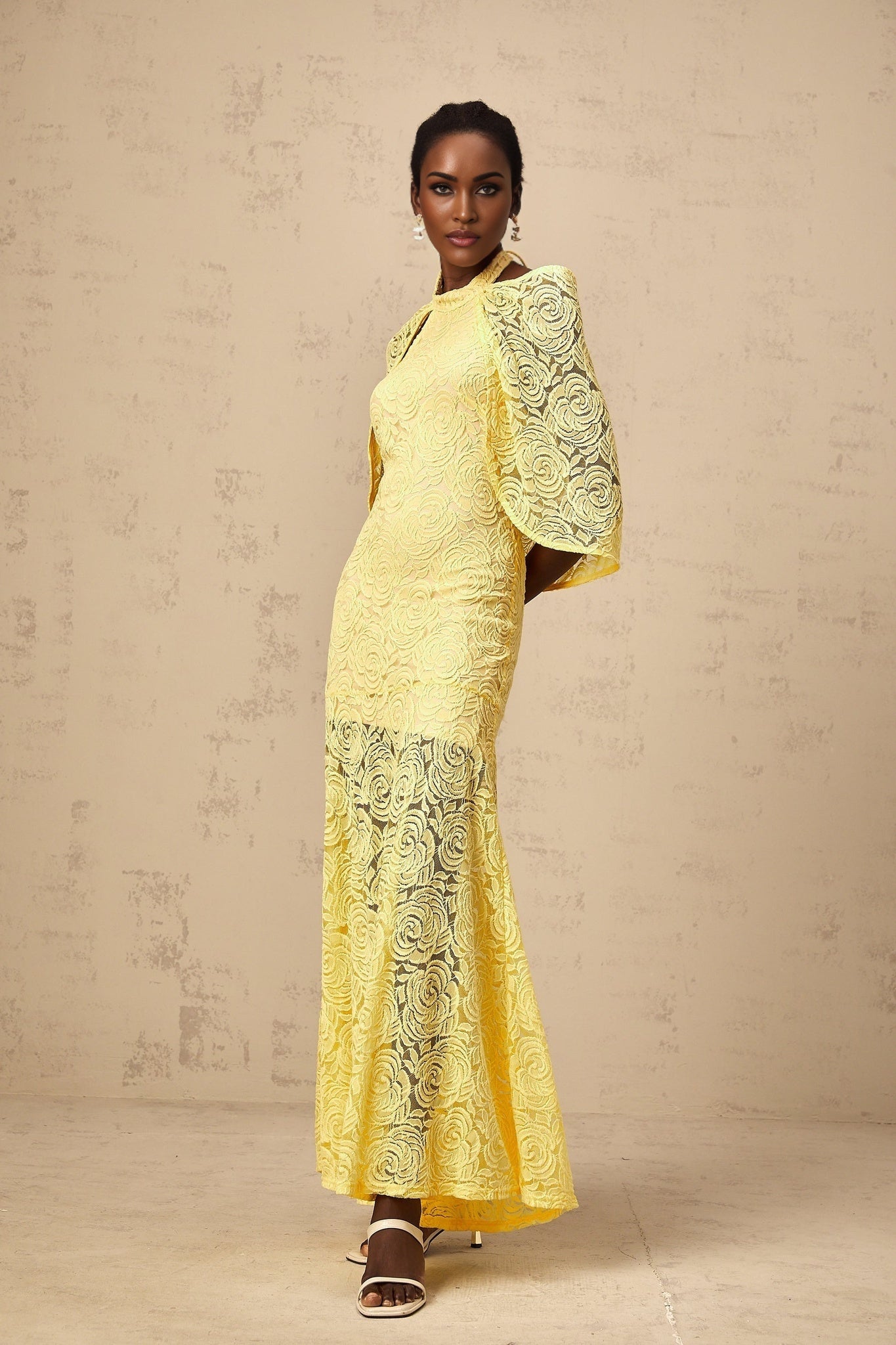 A long yellow maxi dress with a cape design made from delicate chantilly lace featuring a flowing silhouette and feminine details