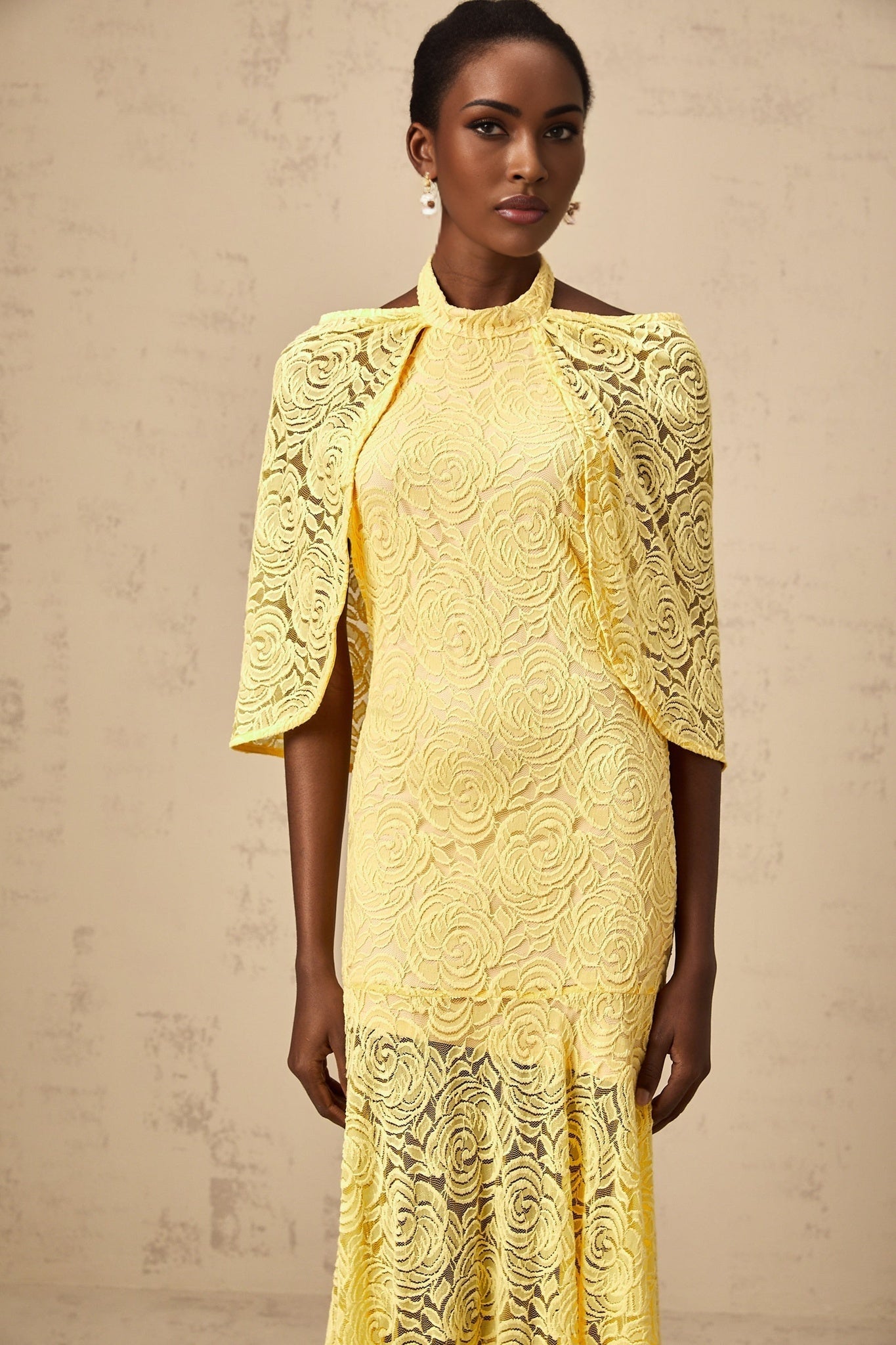 A long yellow maxi dress with a cape design made of delicate chantilly lace featuring an elegant and flowing silhouette