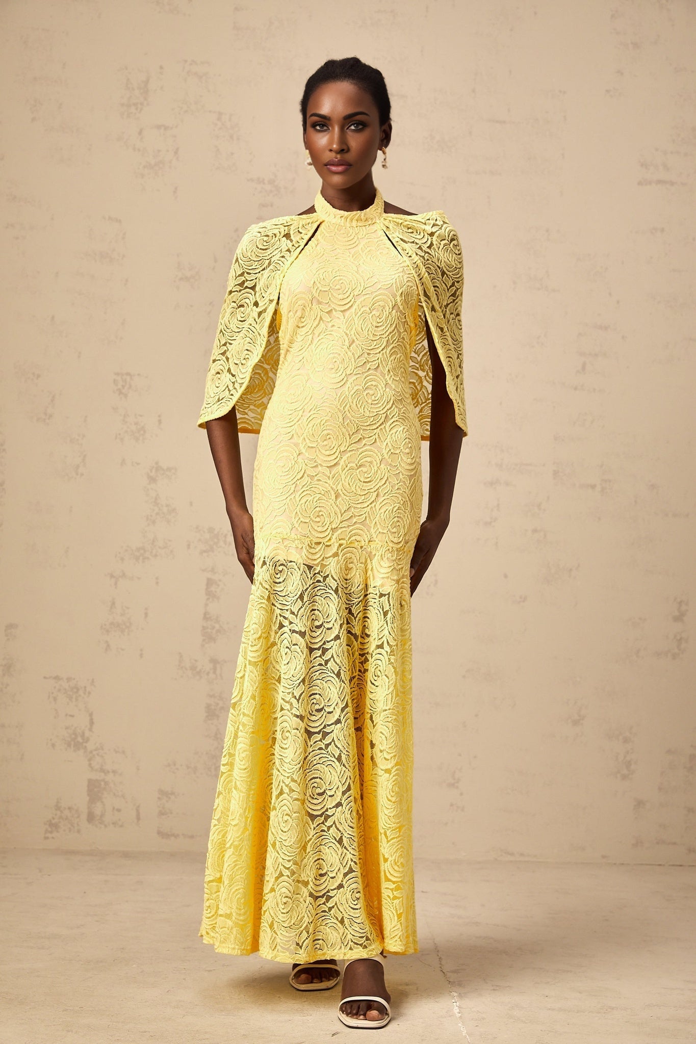 A long yellow maxi dress with a cape design made of delicate chantilly lace featuring an elegant and flowing silhouette