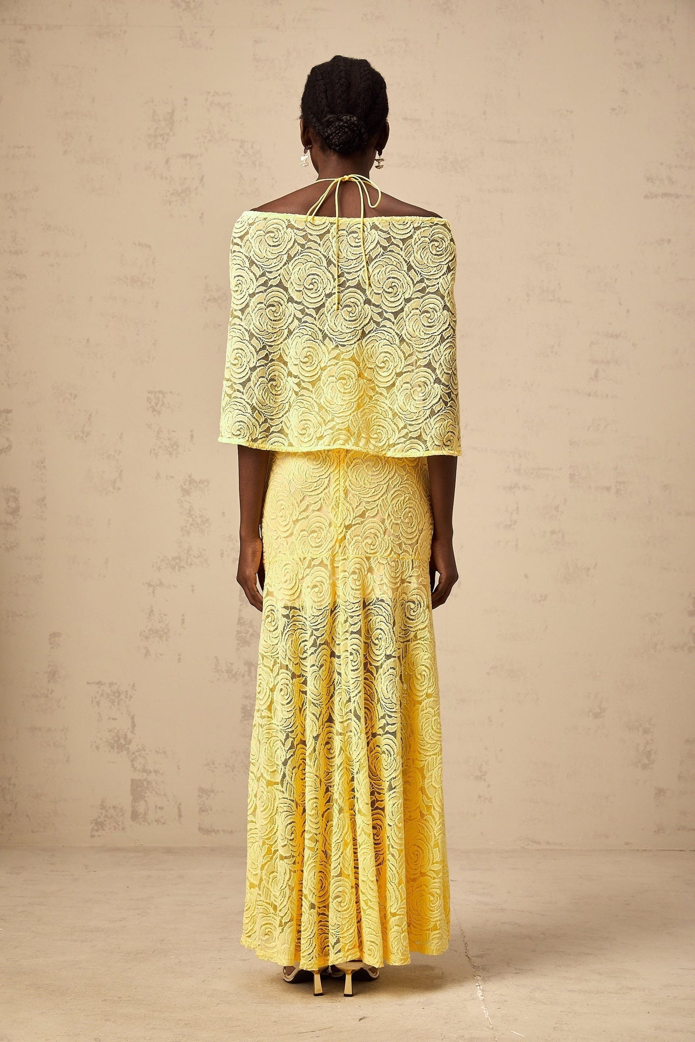 A long yellow maxi dress with a cape design made of delicate chantilly lace featuring an elegant and flowing silhouette