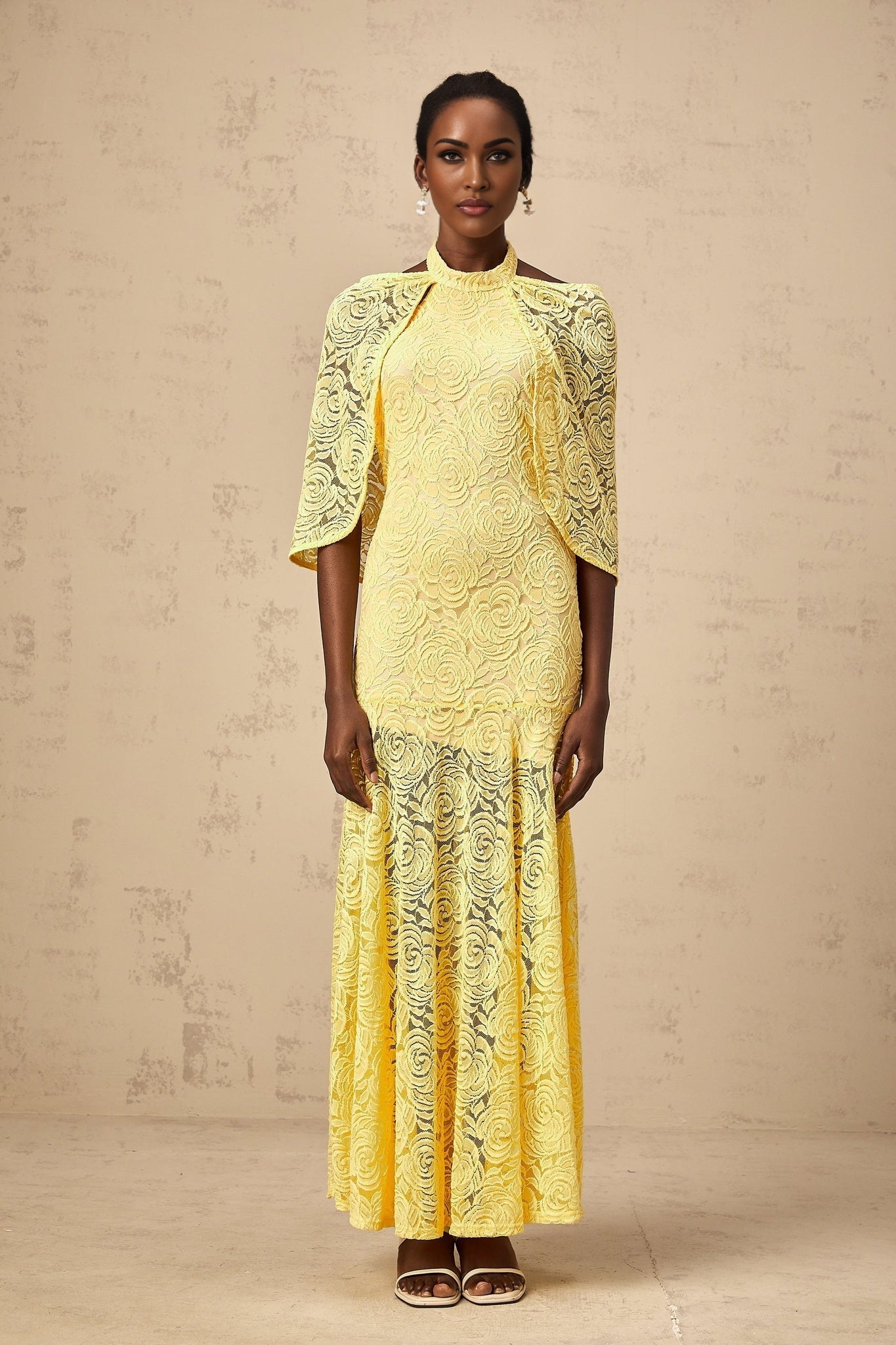 A long yellow maxi dress with a cape design made of delicate chantilly lace featuring an elegant and flowing silhouette