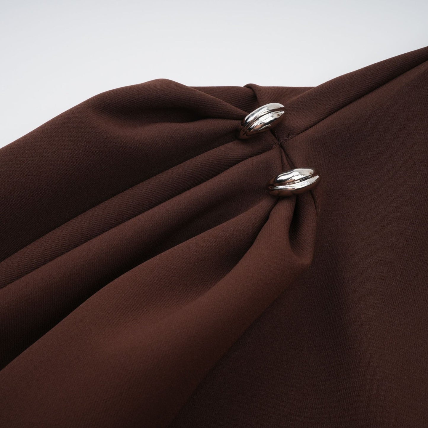 A model wearing a brown asymmetrical midi dress with a fitted bodice and flowing skirt