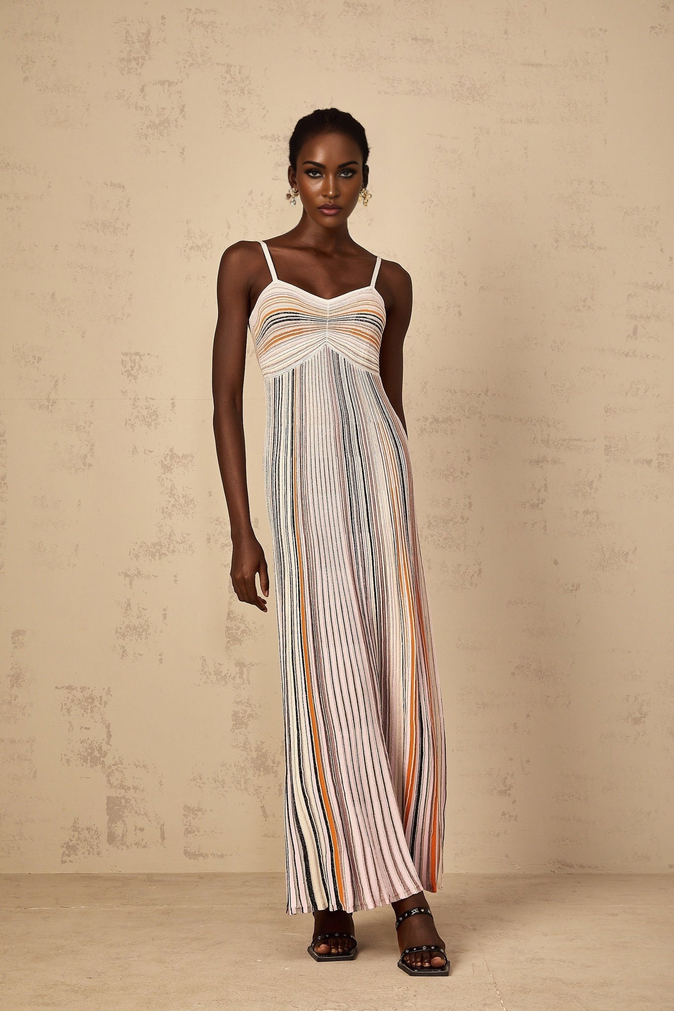 A neutral colored long maxi dress with horizontal stripes of sequins across the knit fabric worn by a woman