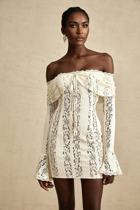 A neutral colored mini dress with flared cuffs featuring a floral lace pattern and named Emeline