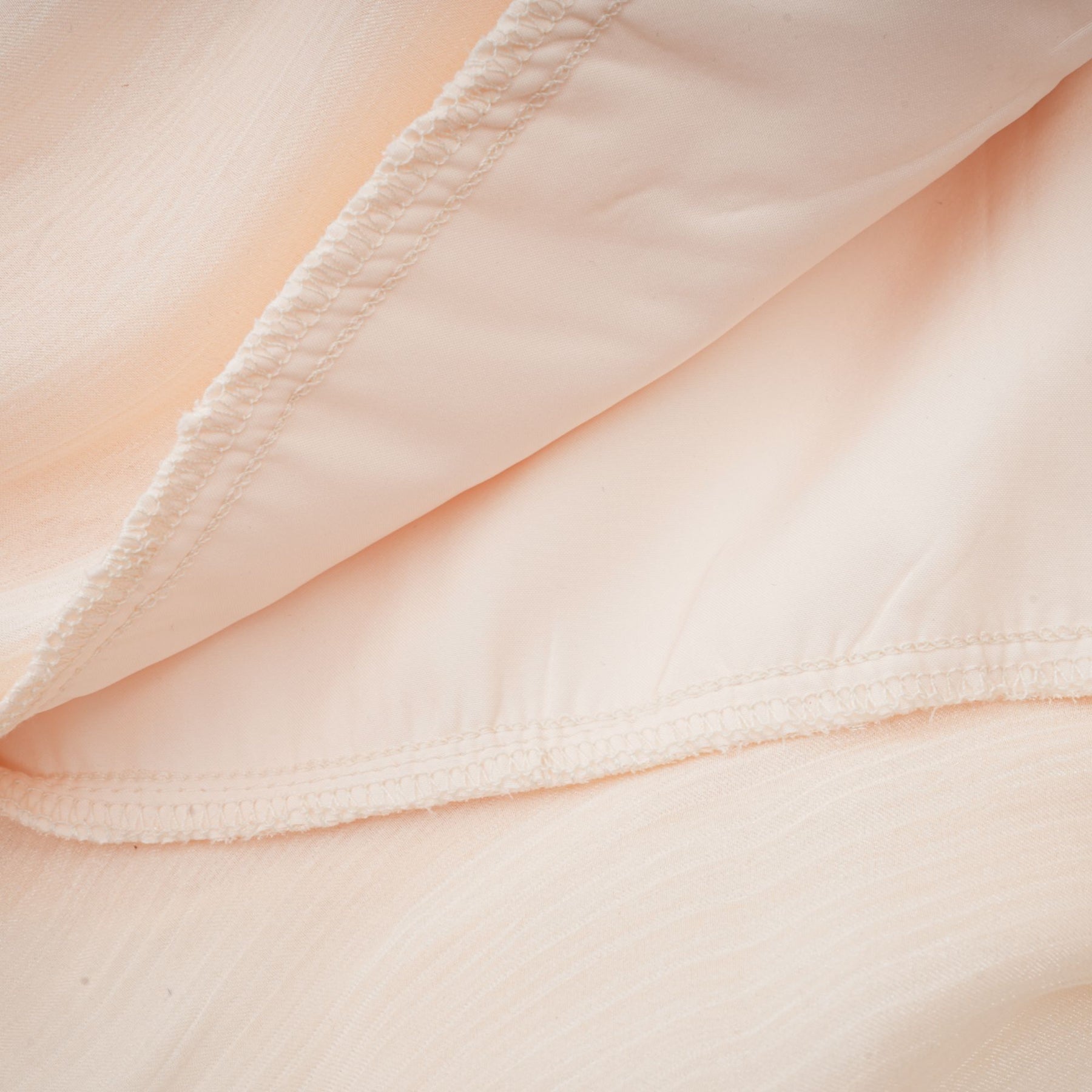 A neutral colored mini dress with full pleats and ruffles featuring a feminine Eugenie style design