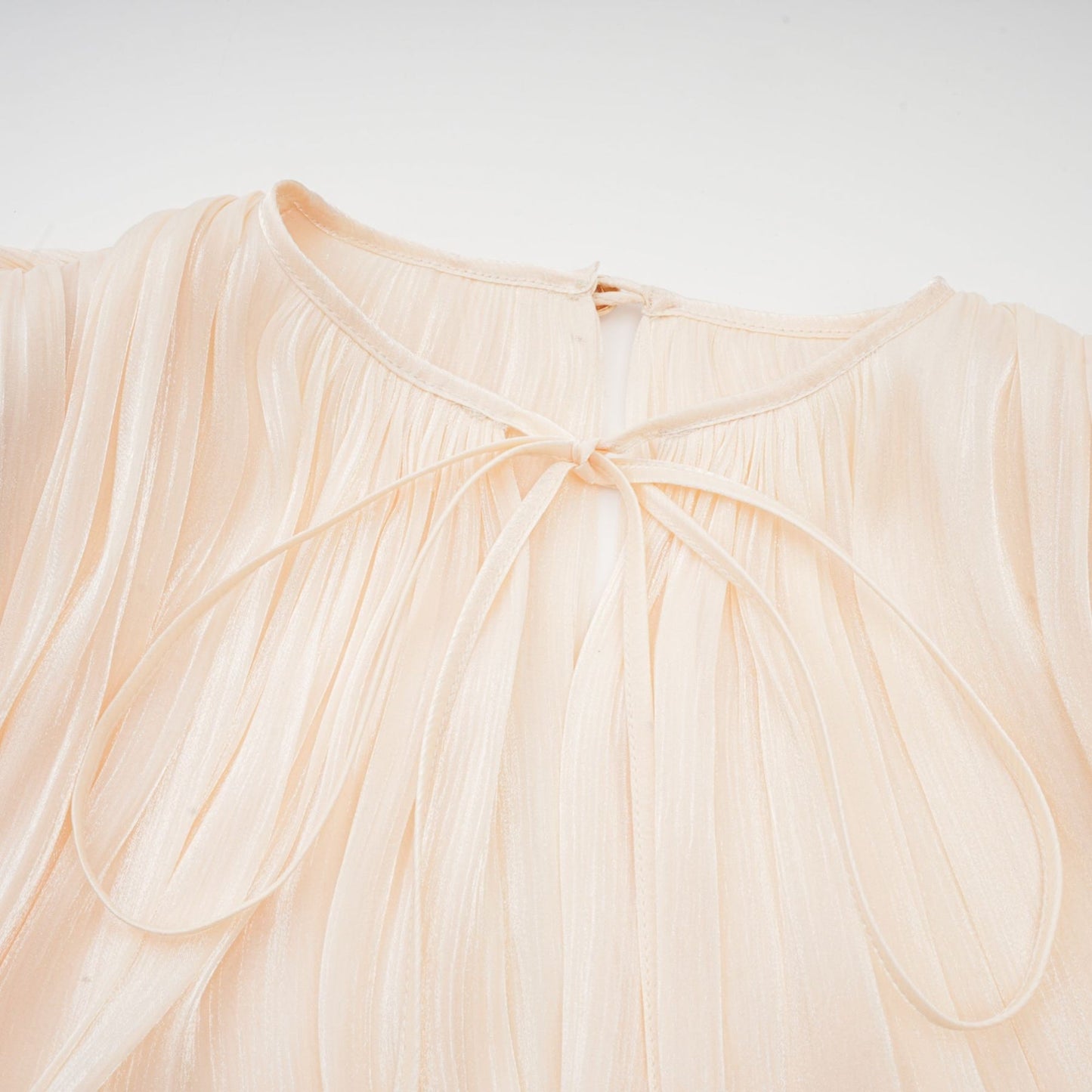 Neutraltoned dress with long sleeves tie neck twist design shoulder pads draped style pleats ruffled hem and shimmer details
