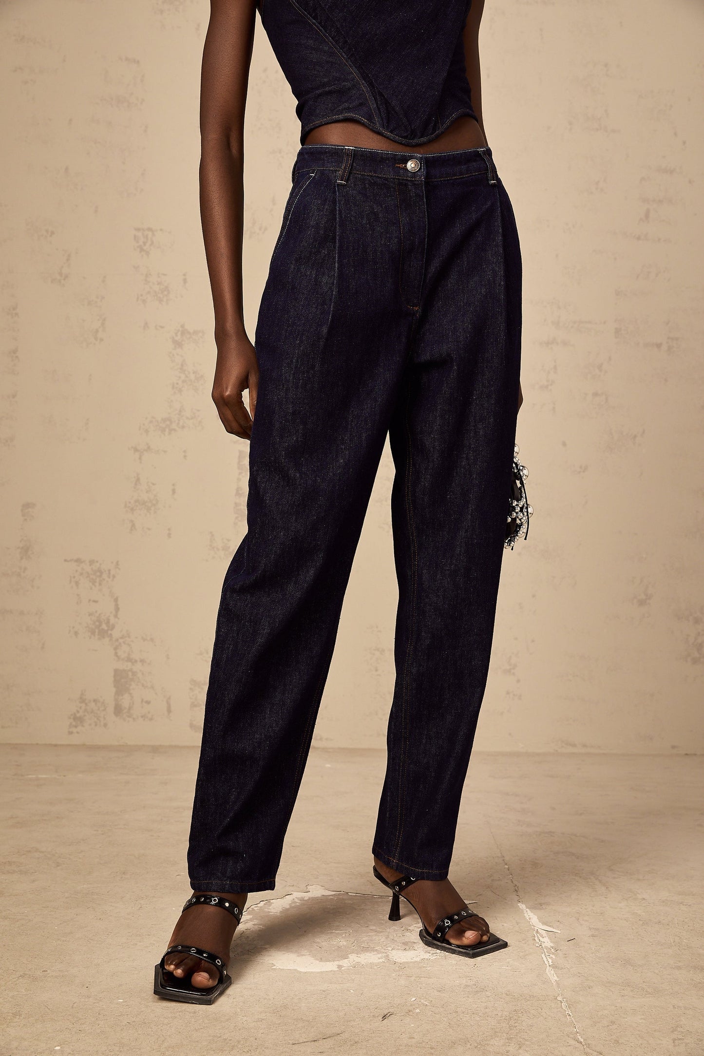 A pair of blue high rise jeans with pleated details on the front featuring a relaxed fit and a light wash denim fabric