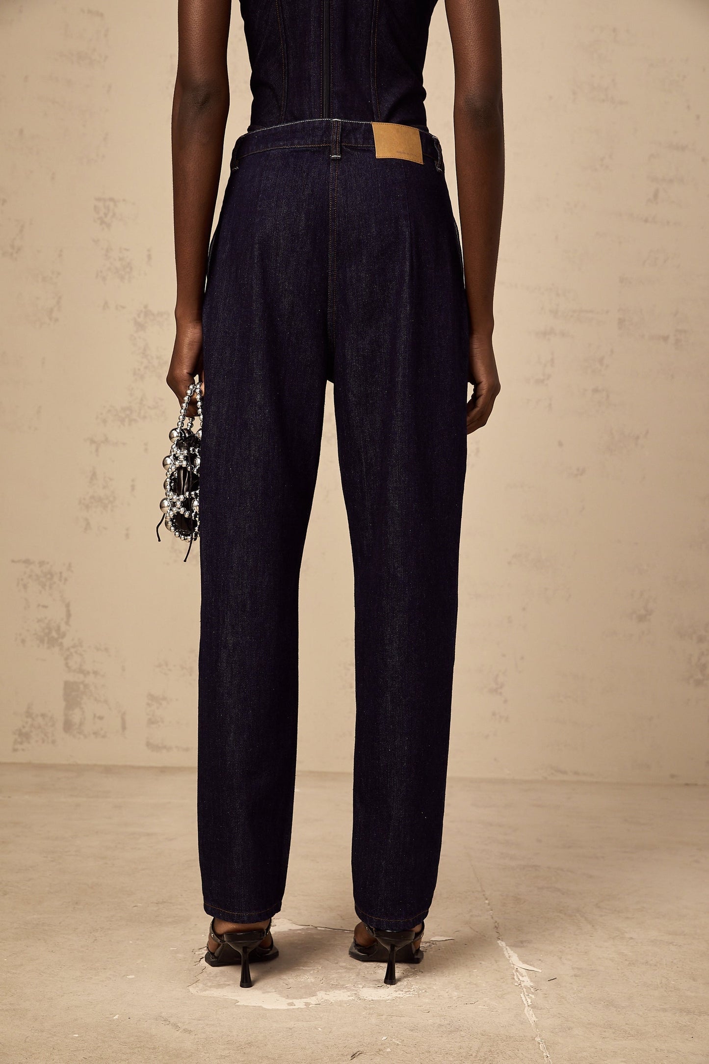A pair of blue high rise jeans with pleated details on the front featuring a relaxed fit and tapered leg
