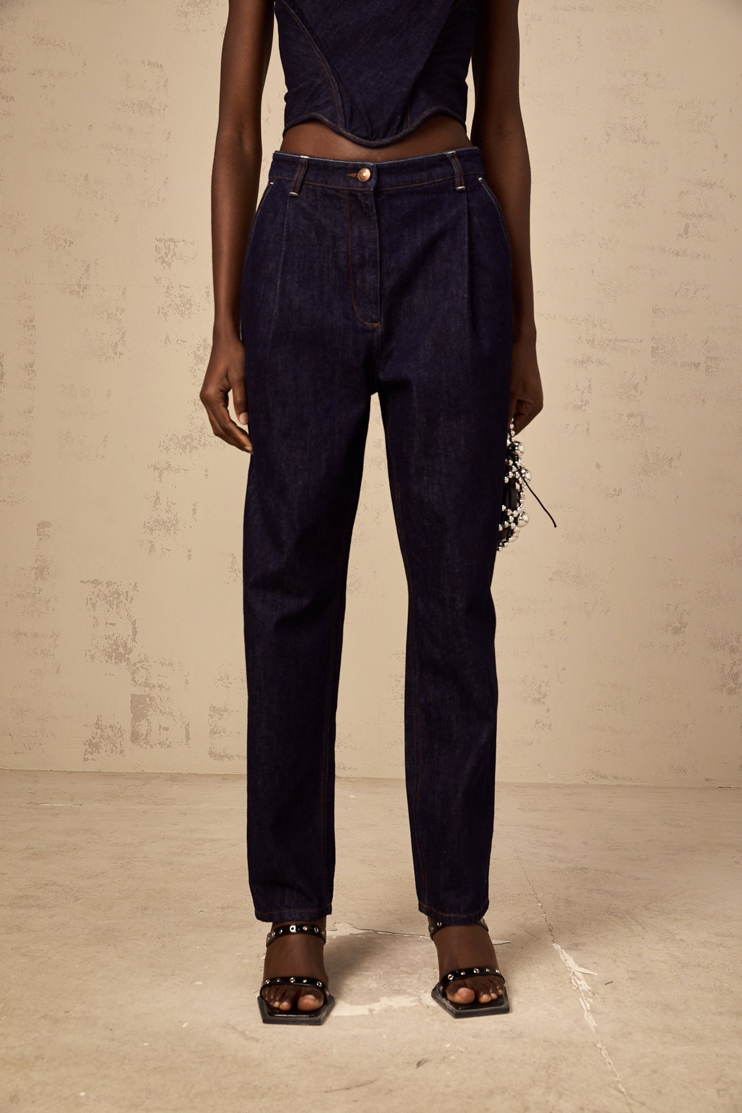 A pair of blue high rise jeans with pleated details on the front named Danae