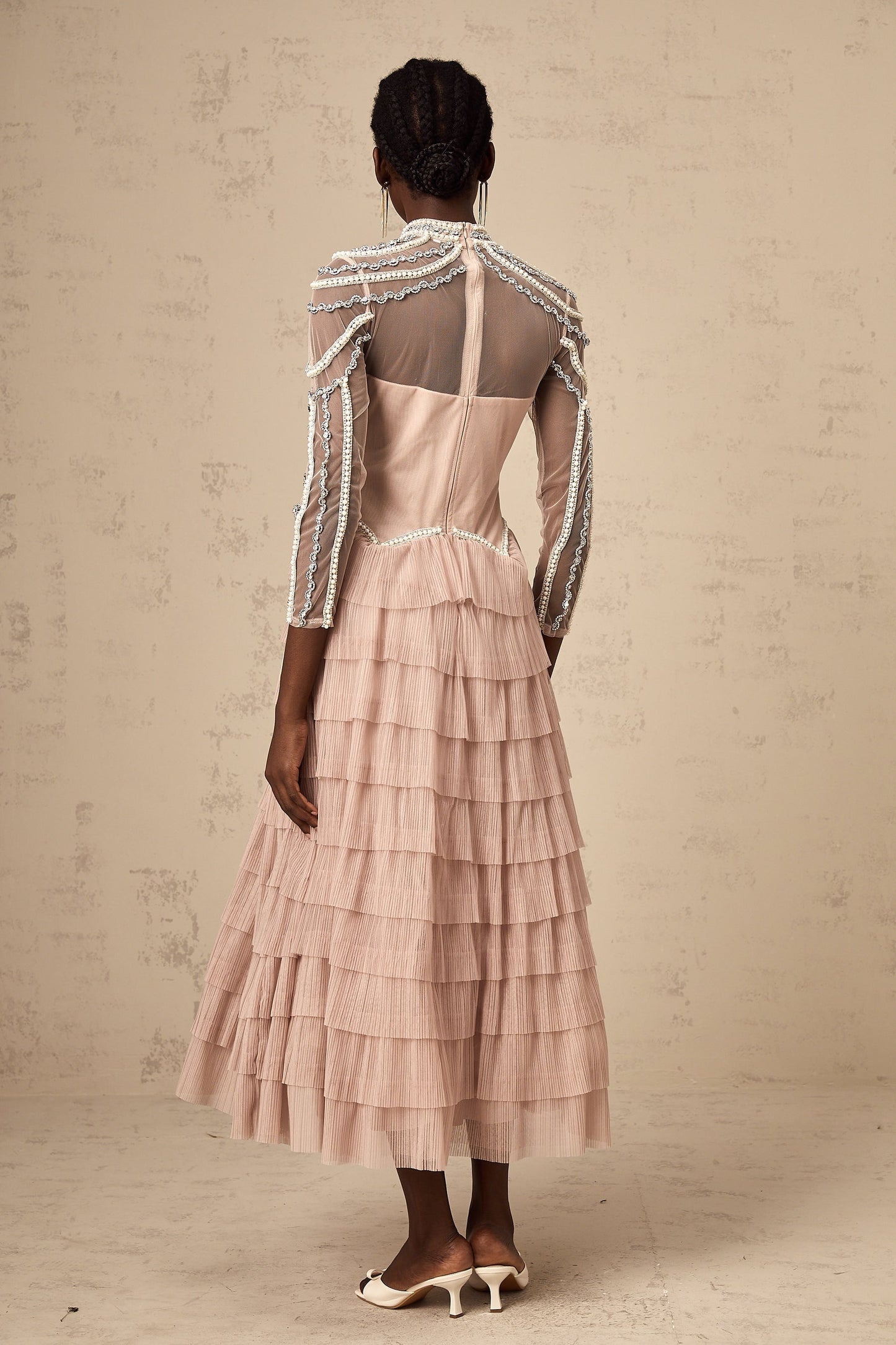 A pink beaded gown with tiered layers and semi sheer fabric featuring a long flowing silhouette