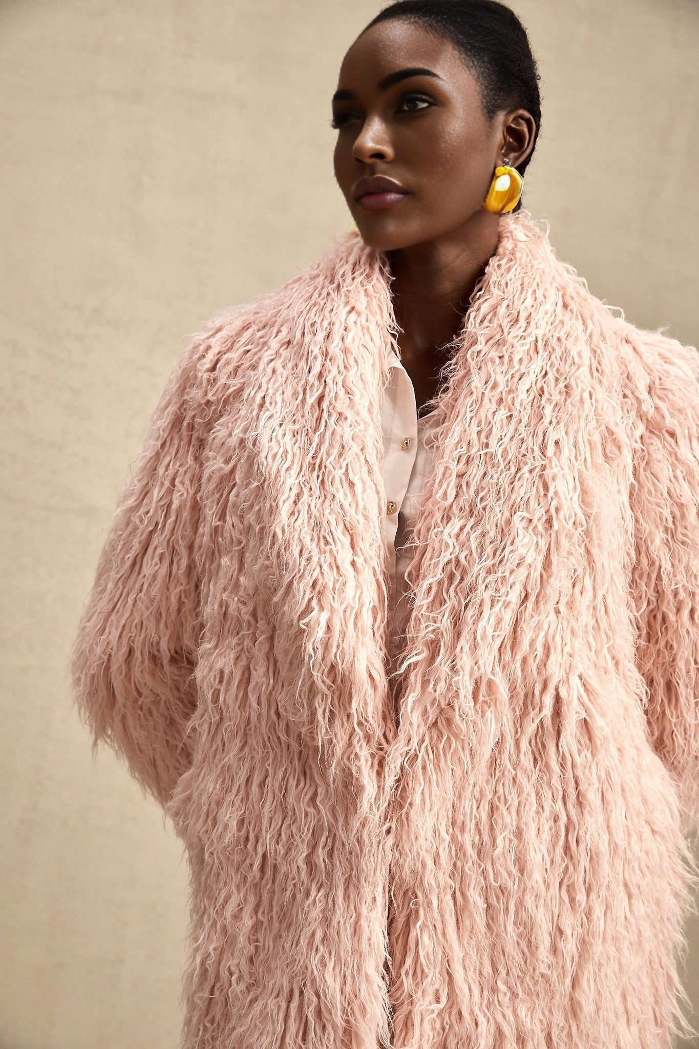 A pink faux fur coat with an open front design modeled by a woman against a plain background