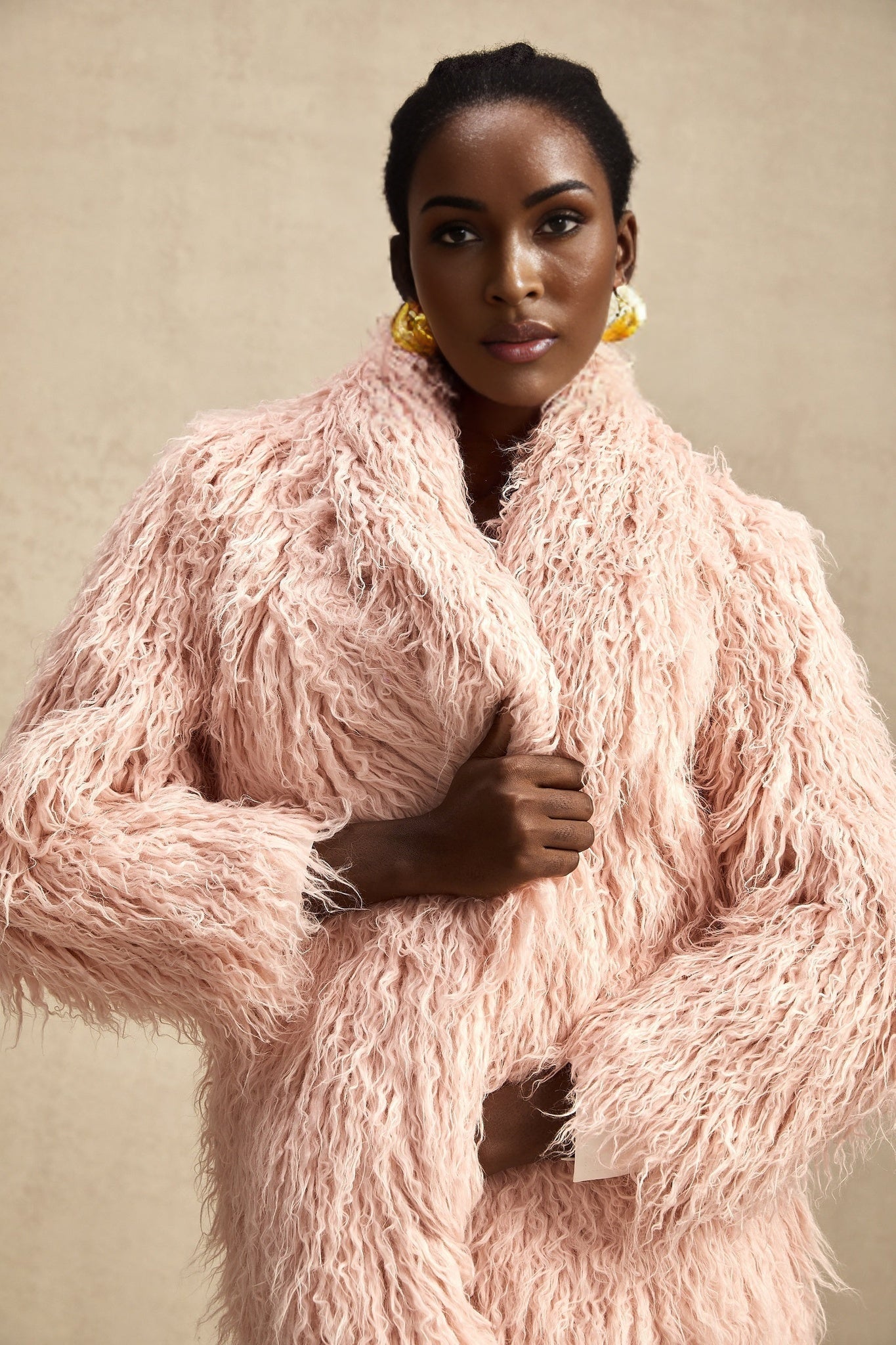 A pink faux fur coat with an open front design worn by a model against a plain background