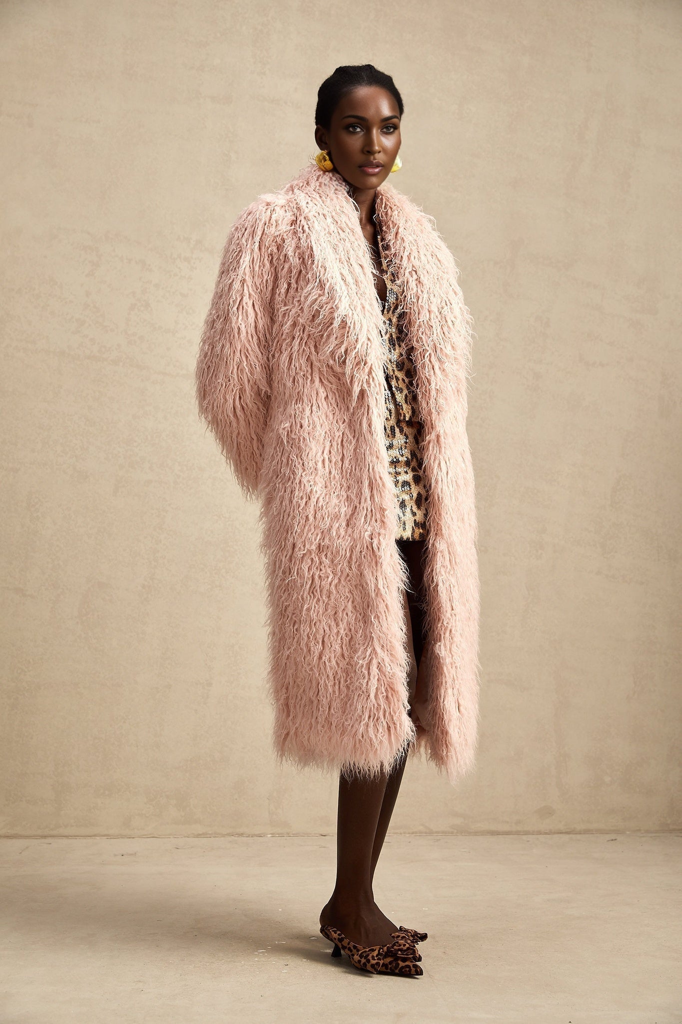 A pink faux fur coat with an open front design worn by a model against a plain background