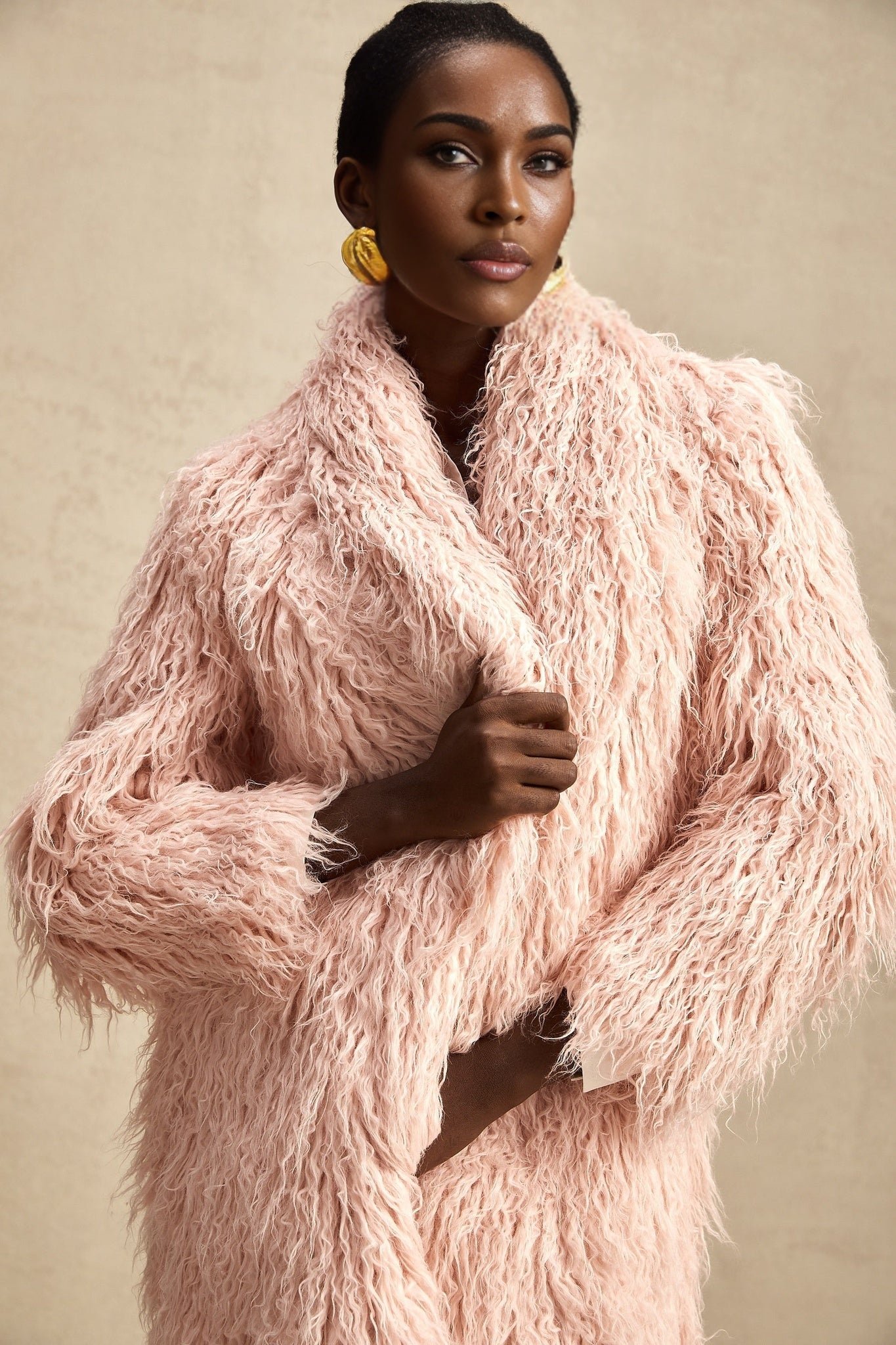 A pink faux fur coat with an open front design worn by a model standing against a plain background