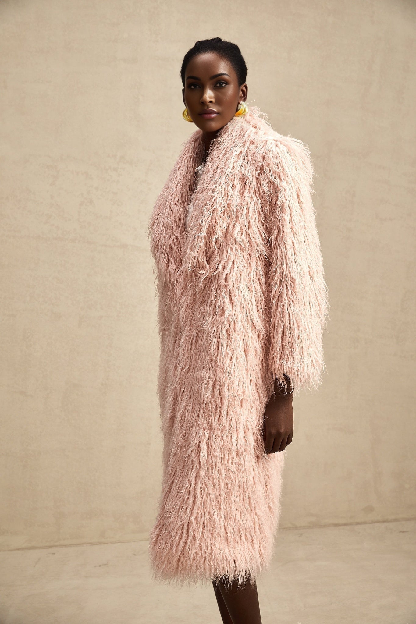 A pink faux fur coat with an open front design worn by a model standing against a plain background