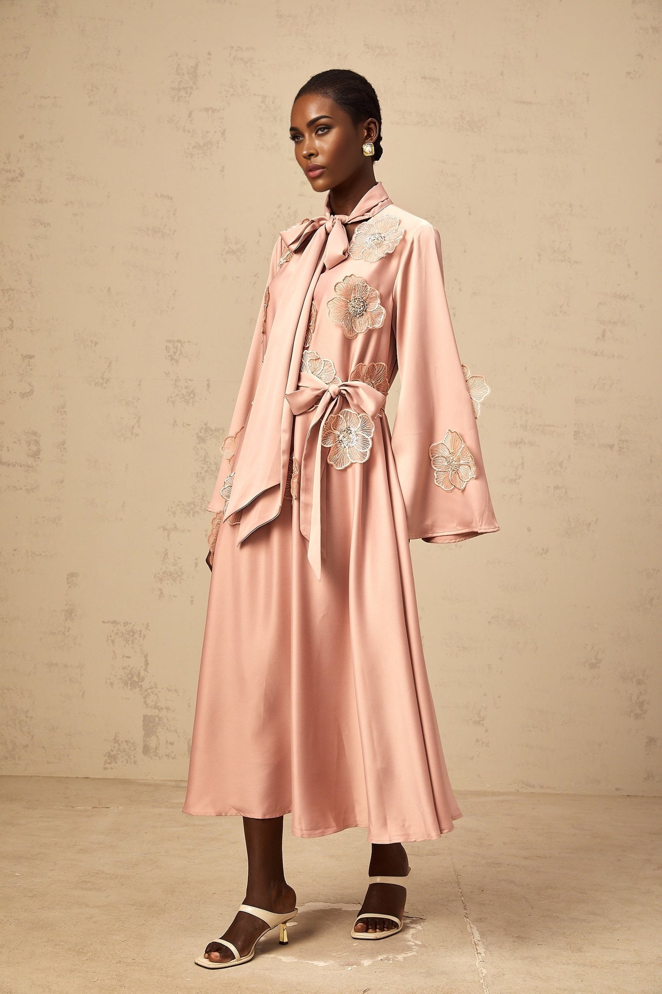 A pink flared midi dress with floral applique details and a tied waist featuring a vibrant orange hue and feminine silhouette