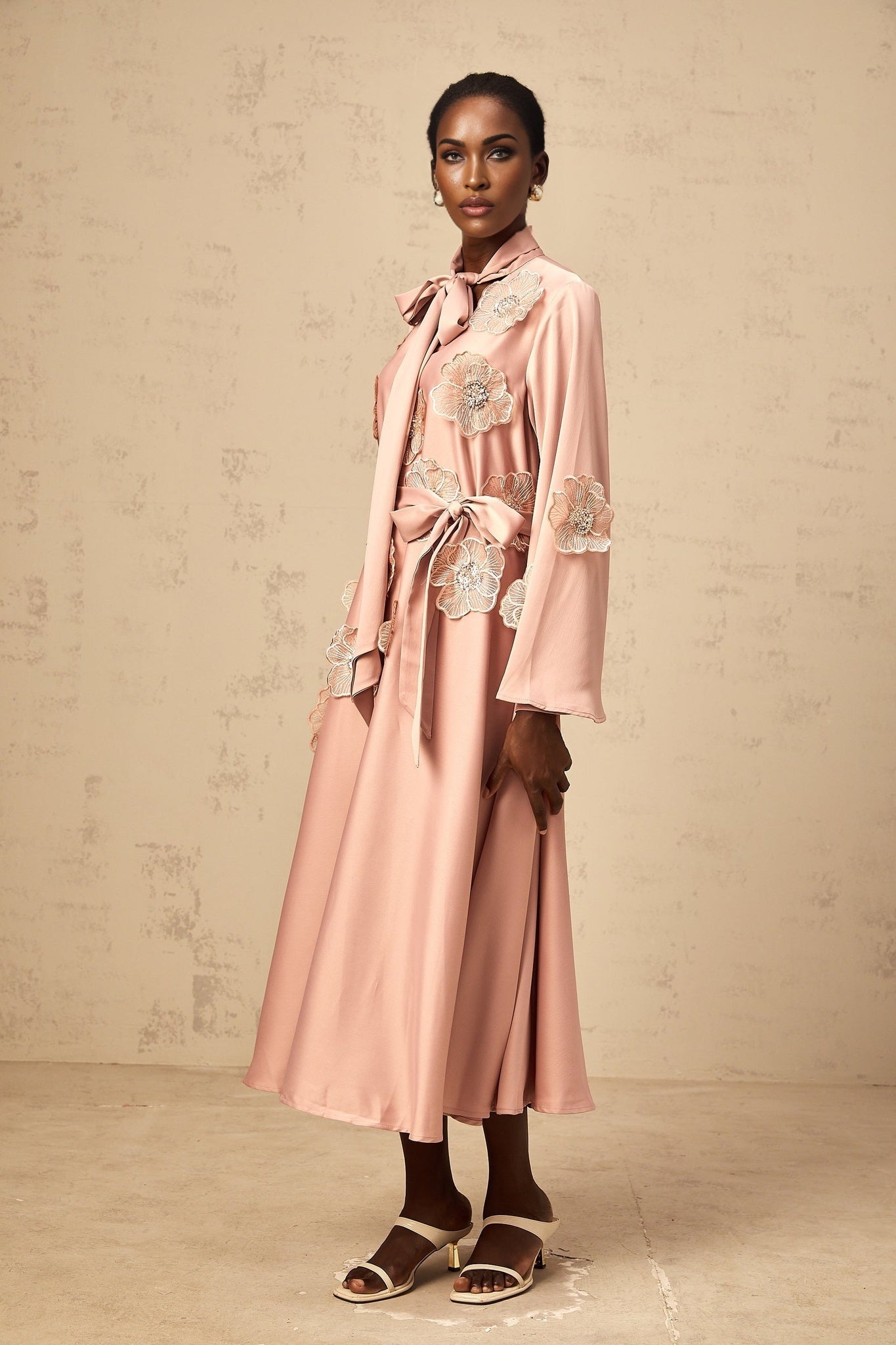 A pink flared midi dress with tie detail and floral applique decorations