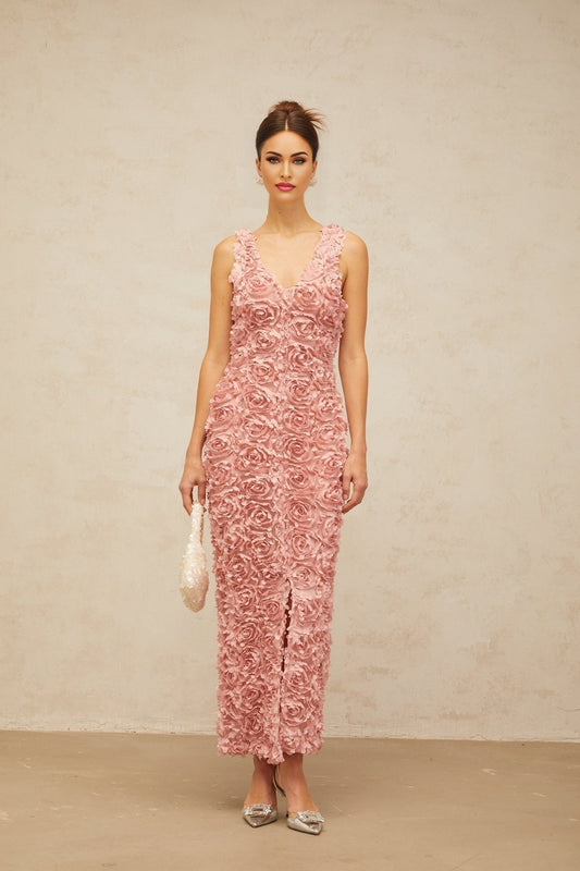 A pink floral maxi dress with a Vneck and faux flower details worn by a model standing against a plain background