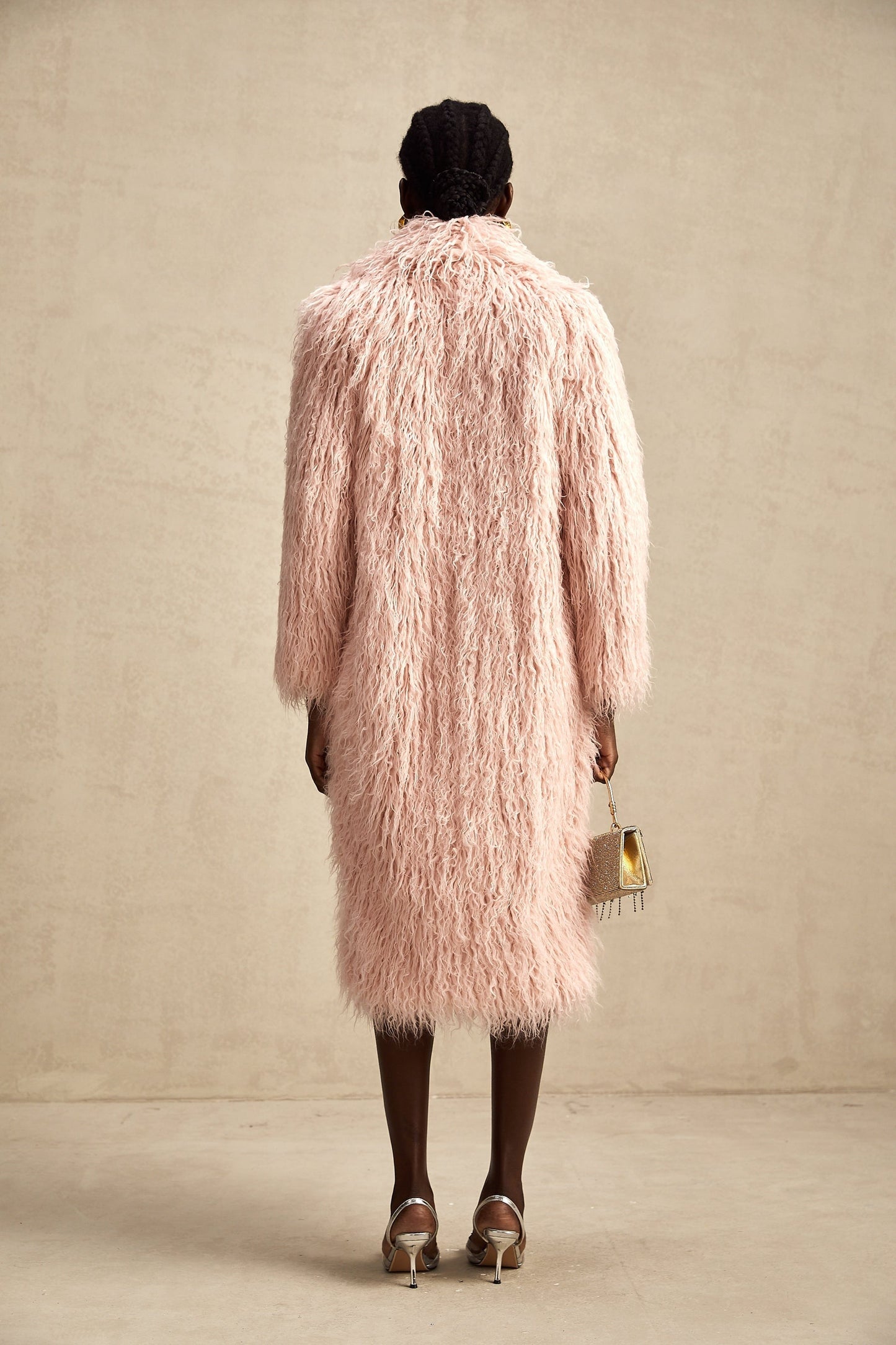 A pink fluffy faux fur coat with an open front design worn by a model standing against a plain background