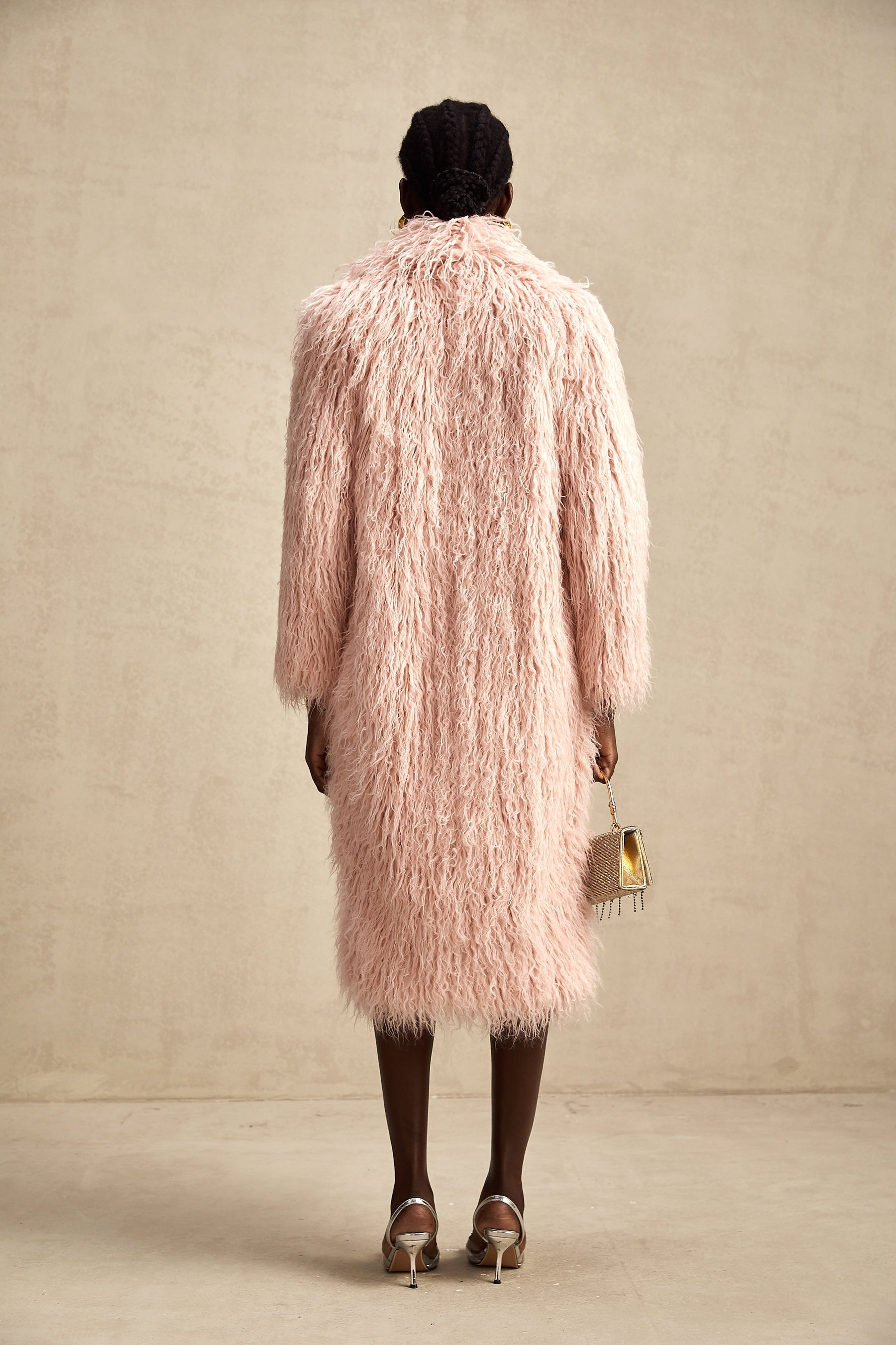 A pink fluffy faux fur coat with an open front design worn by a model standing against a plain background