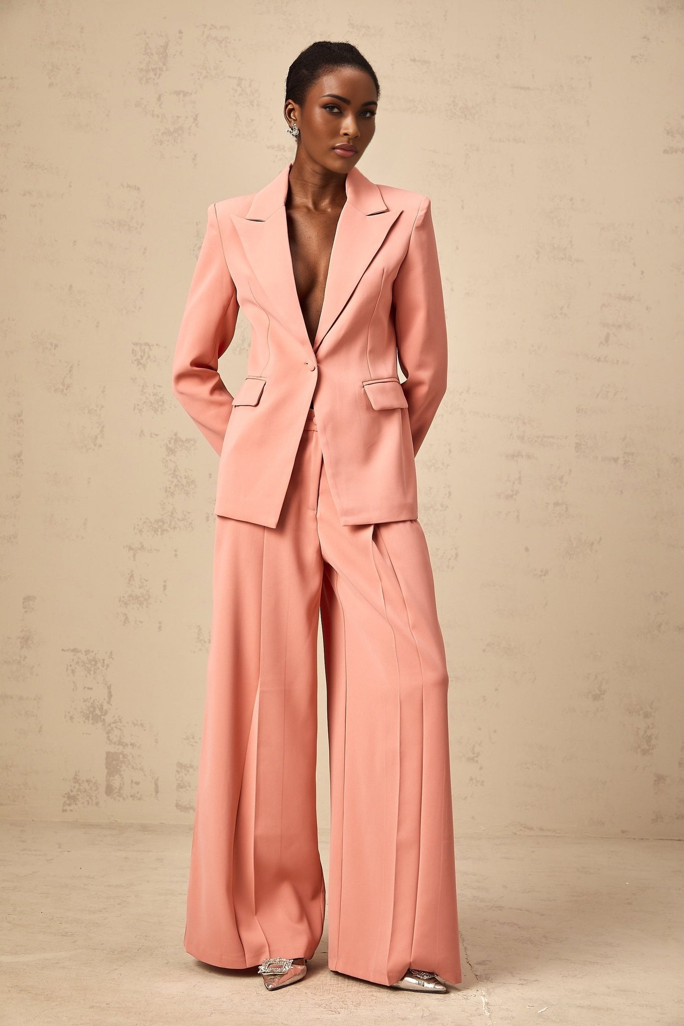 A pink matching set featuring a blazer and trousers with embroidery details and cutout design The blazer has an open front while the trousers are tailored Both pieces have decorative embroidery and strategic cutouts for a stylish look
