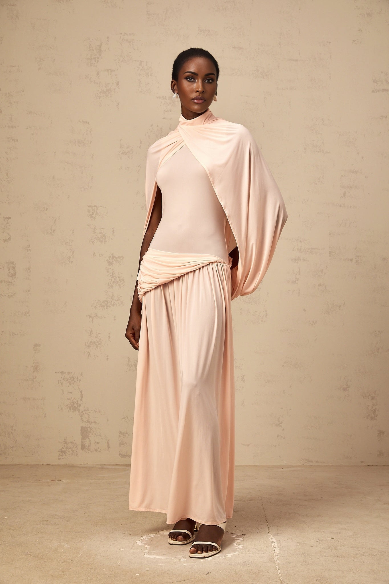 A pink maxi dress with an asymmetrical hemline and capelike design draped over the shoulders