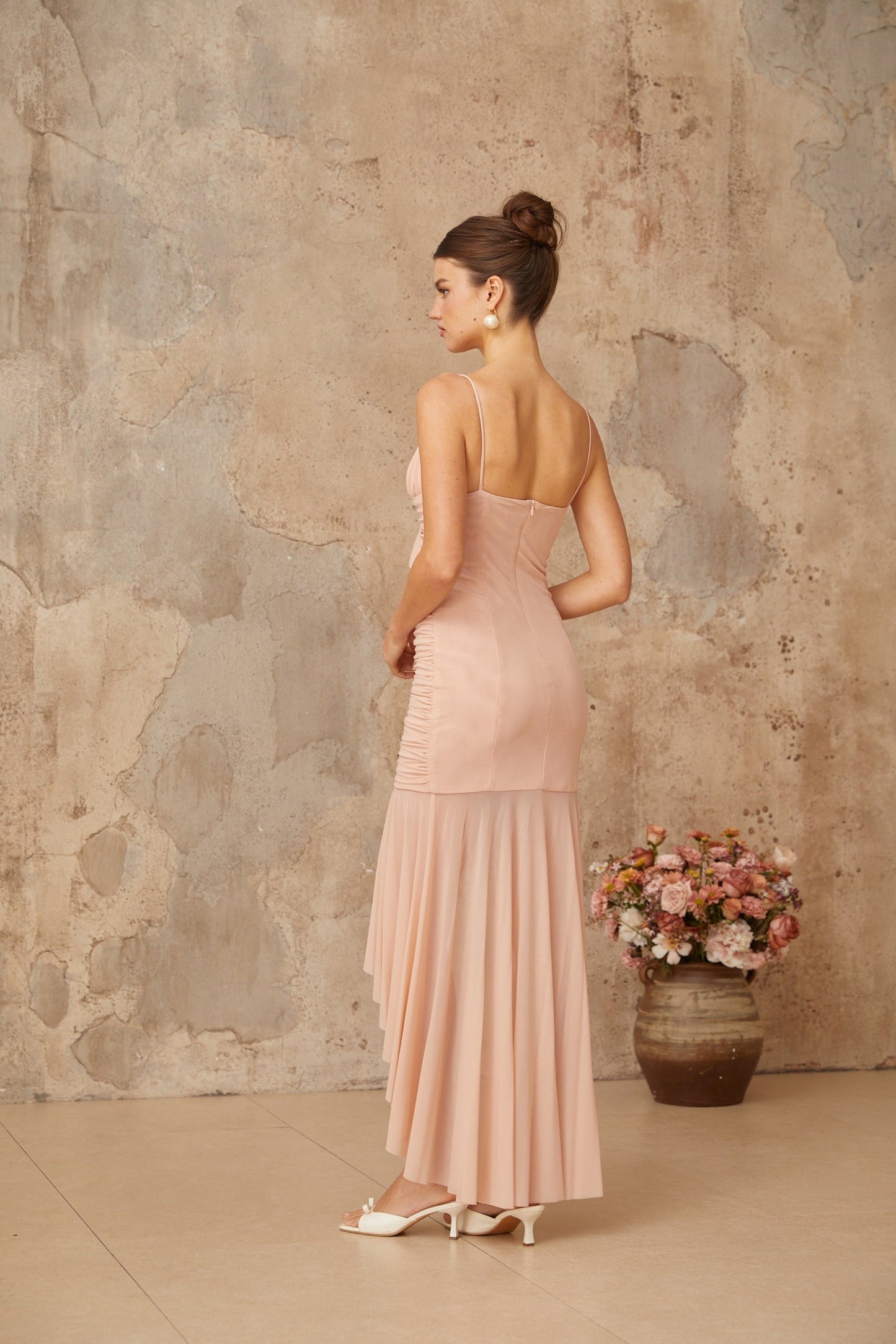 A pink midi dress with asymmetrical ruching and a formfitting silhouette featuring a sleeveless design and a side slit