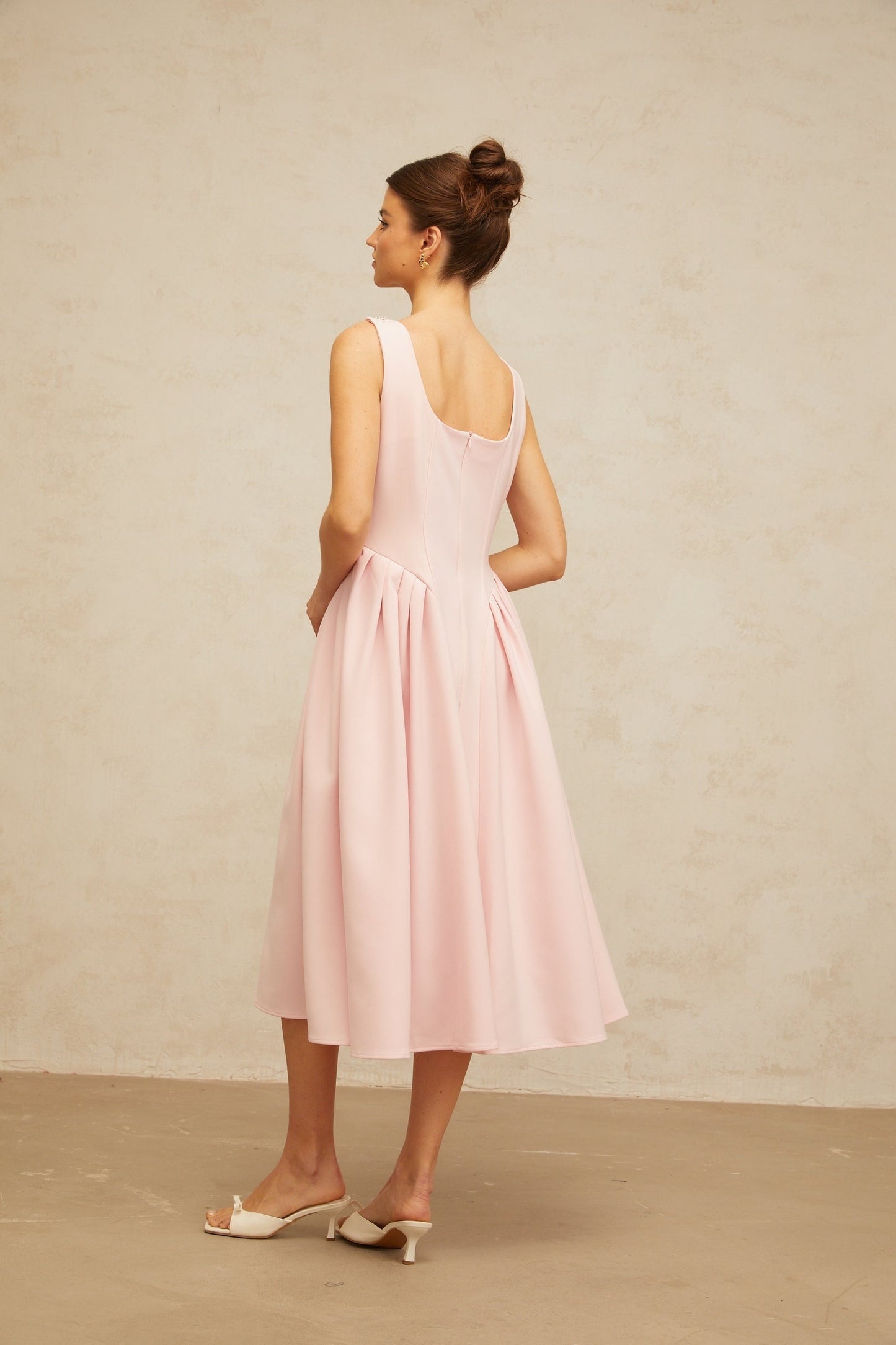 A pink midi dress with crystal embellishments and pleated details featuring a flowy silhouette and elegant design