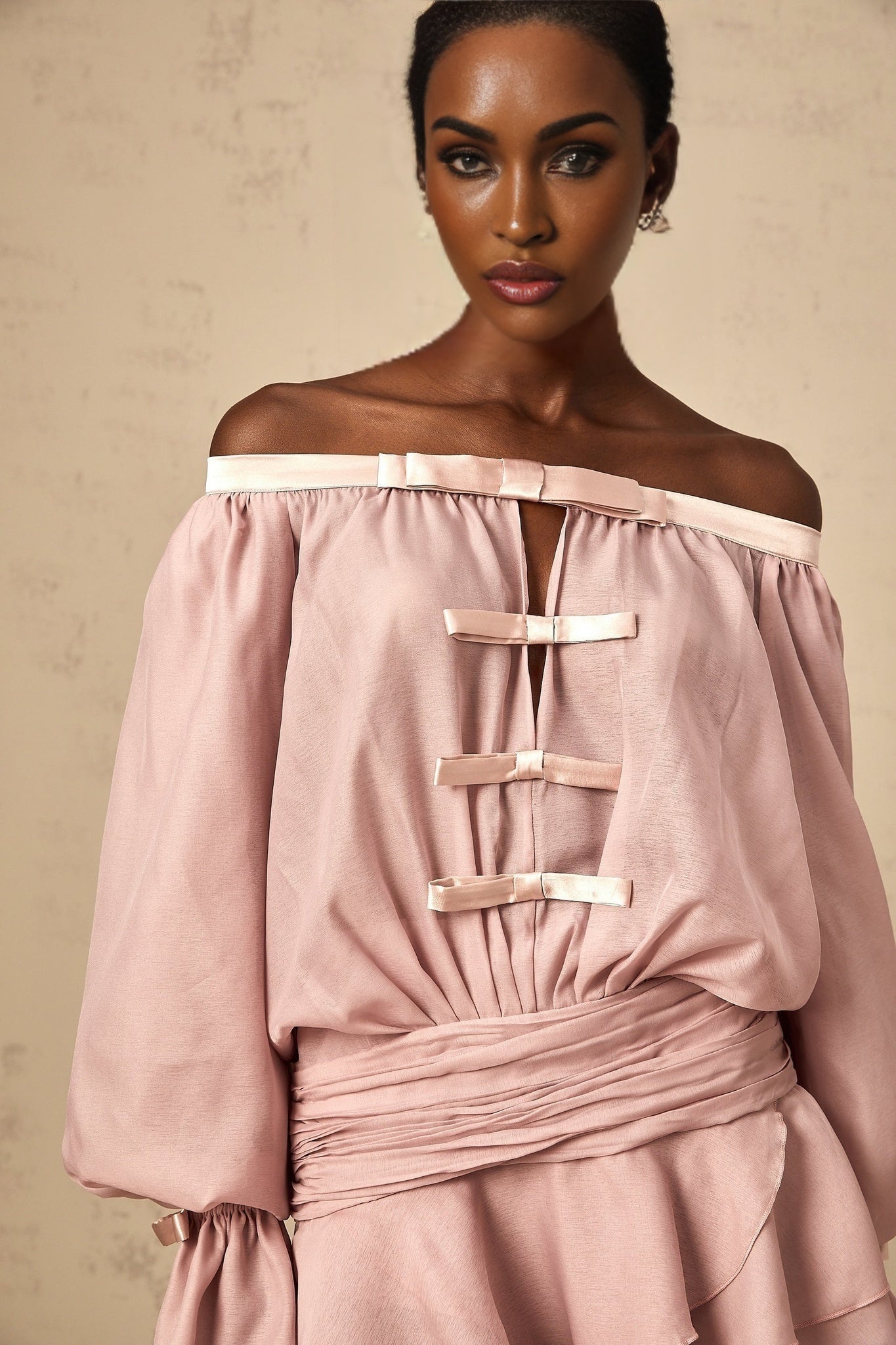 A pink offshoulder mini dress with a bow detail and ruffled hem