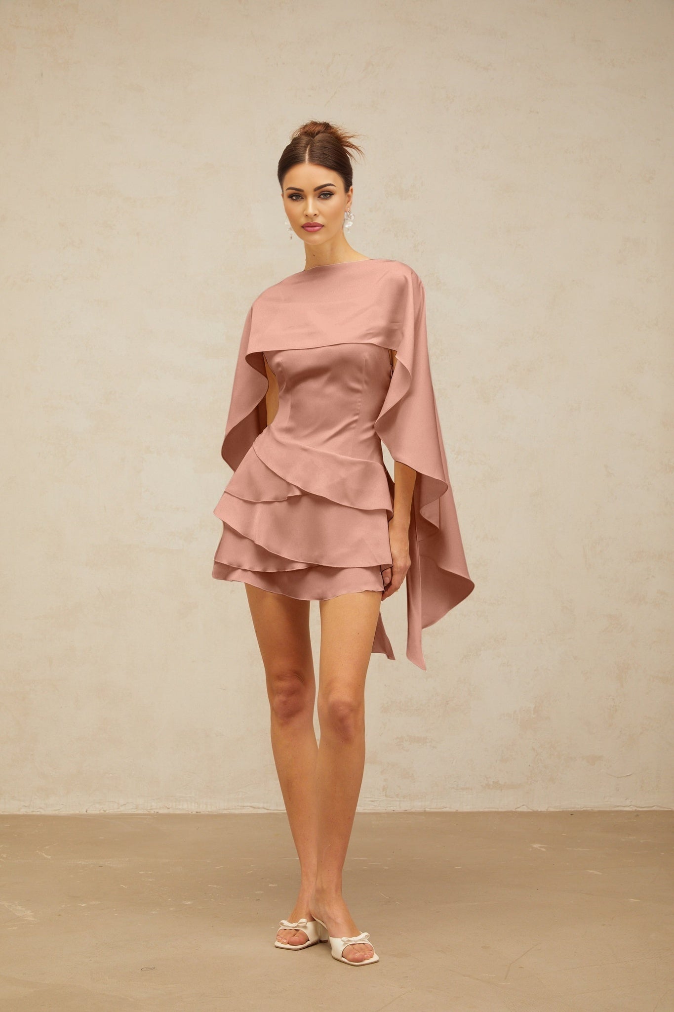 A pink satin mini dress with ruffled details and a shawl panel draping over the shoulders