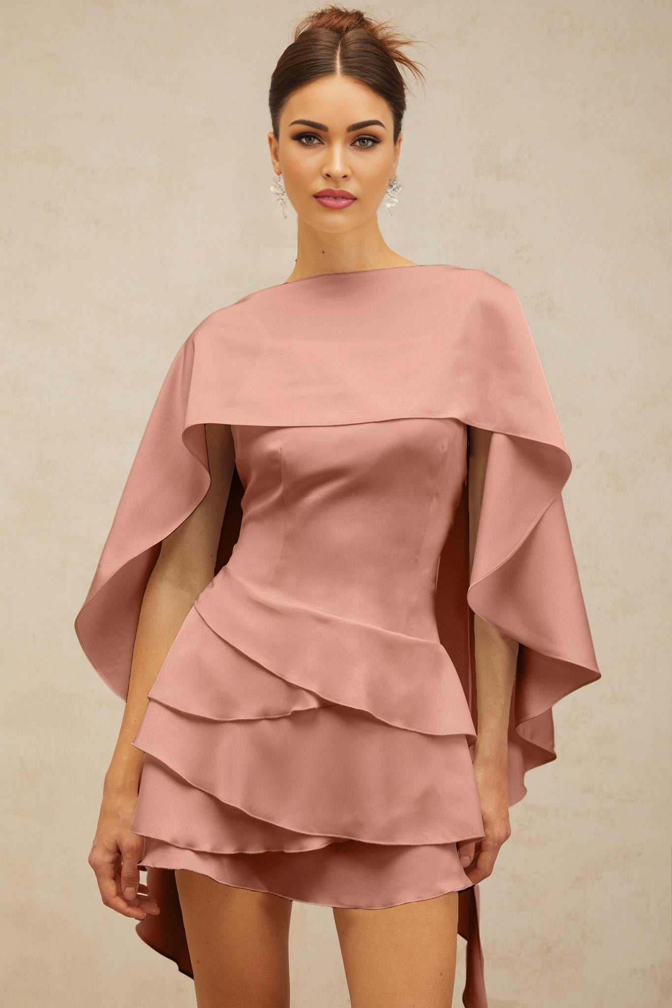 A pink satin mini dress with ruffles and a shawl panel worn by a model standing against a plain background