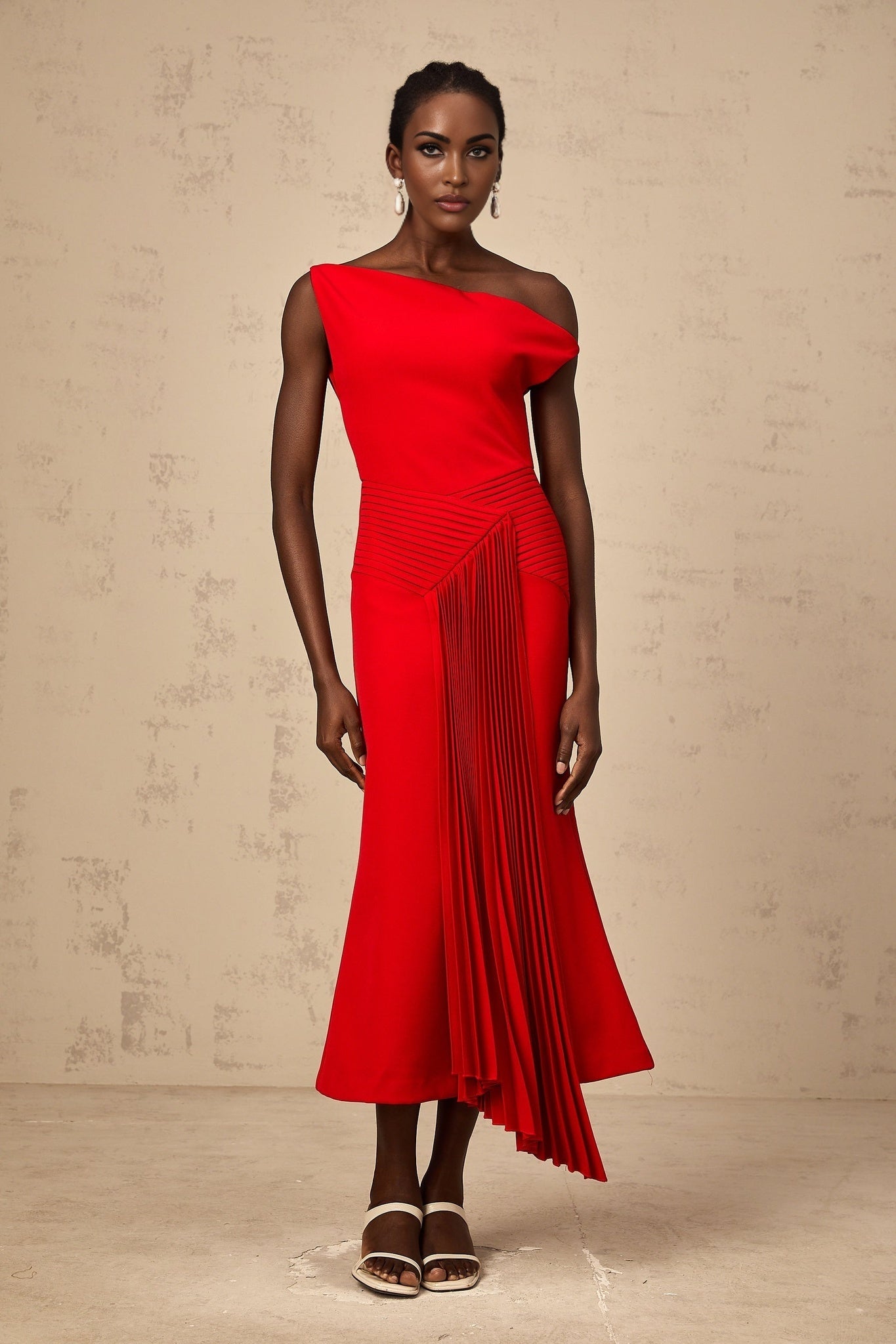 A red asymmetric midi dress with draped fabric details and an uneven hemline worn by a model against a plain background