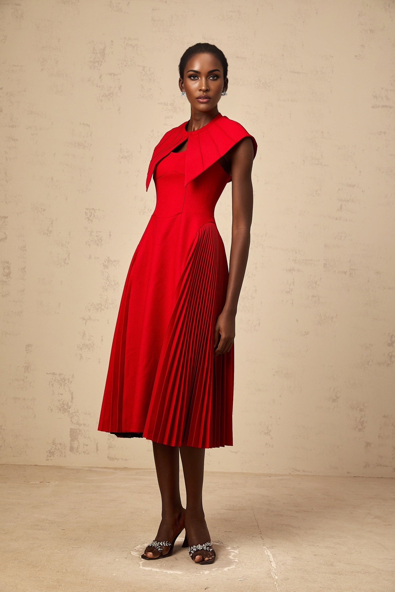 A red midi dress with a capelike design and pleated skirt featuring an amaryllis floral pattern