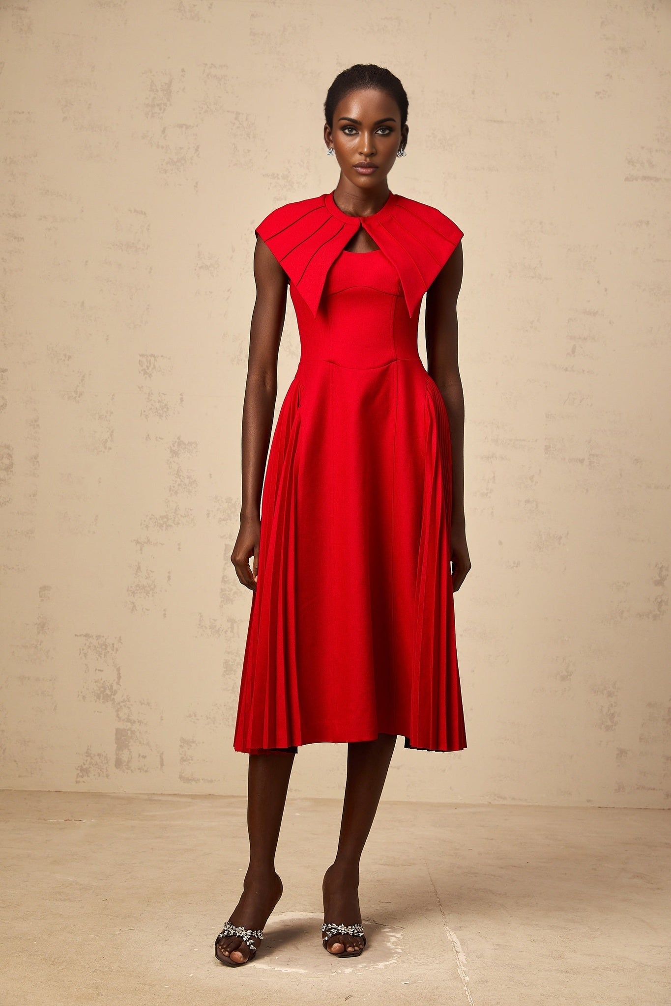 A red midi dress with a capelike design and pleated skirt featuring an amaryllis inspired style