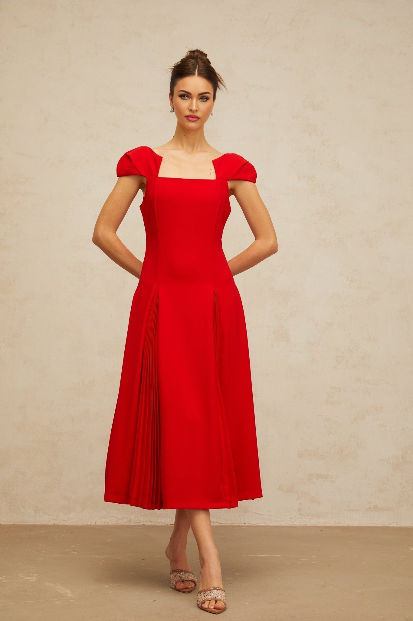 A red midi dress with pleated details and a flared skirt worn by a model standing against a plain background
