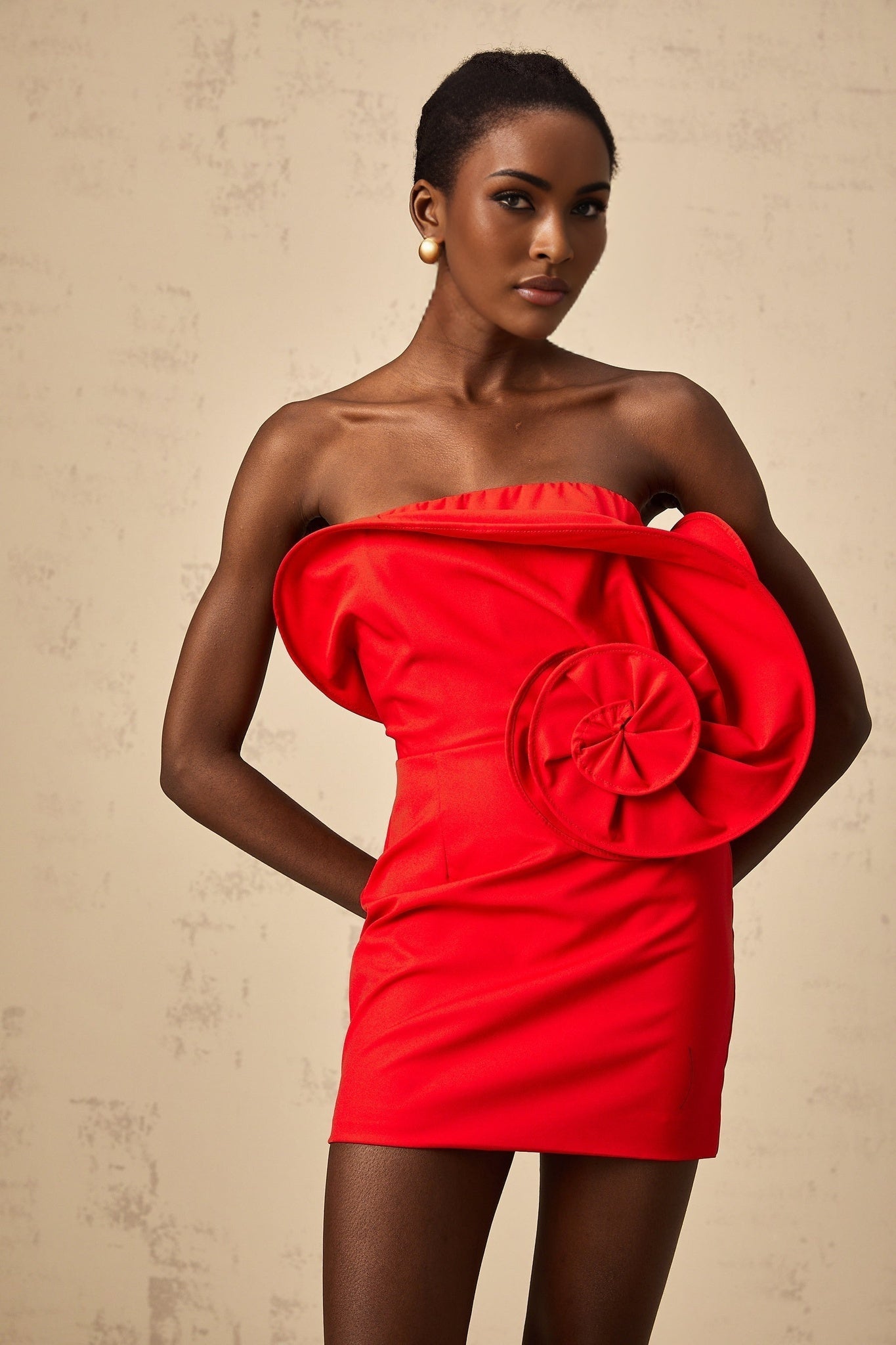 A red mini dress with an offshoulder neckline featuring a large sculptural rose detail on the bodice