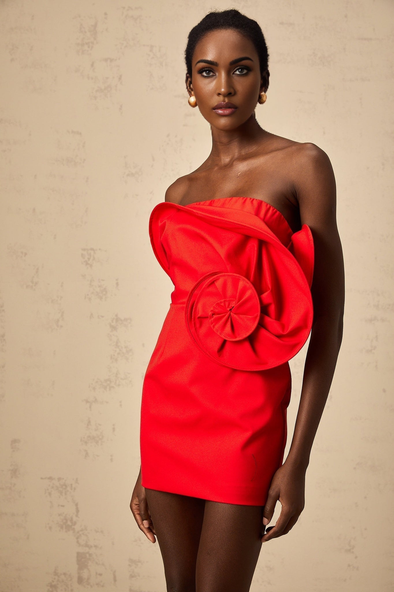 A red mini dress with an offshoulder neckline featuring a large sculptural rose detail on the bodice