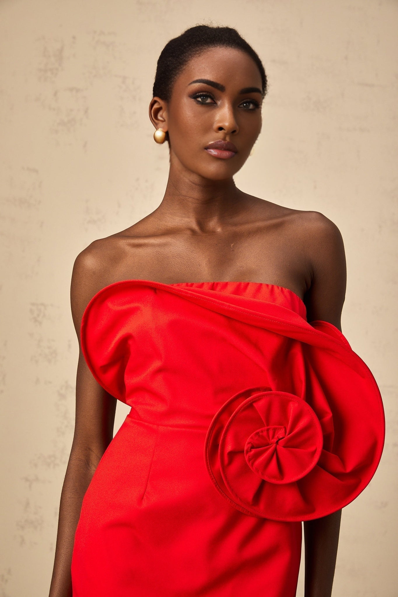 A red mini dress with an offshoulder neckline featuring a large sculptural rose detail on the bodice