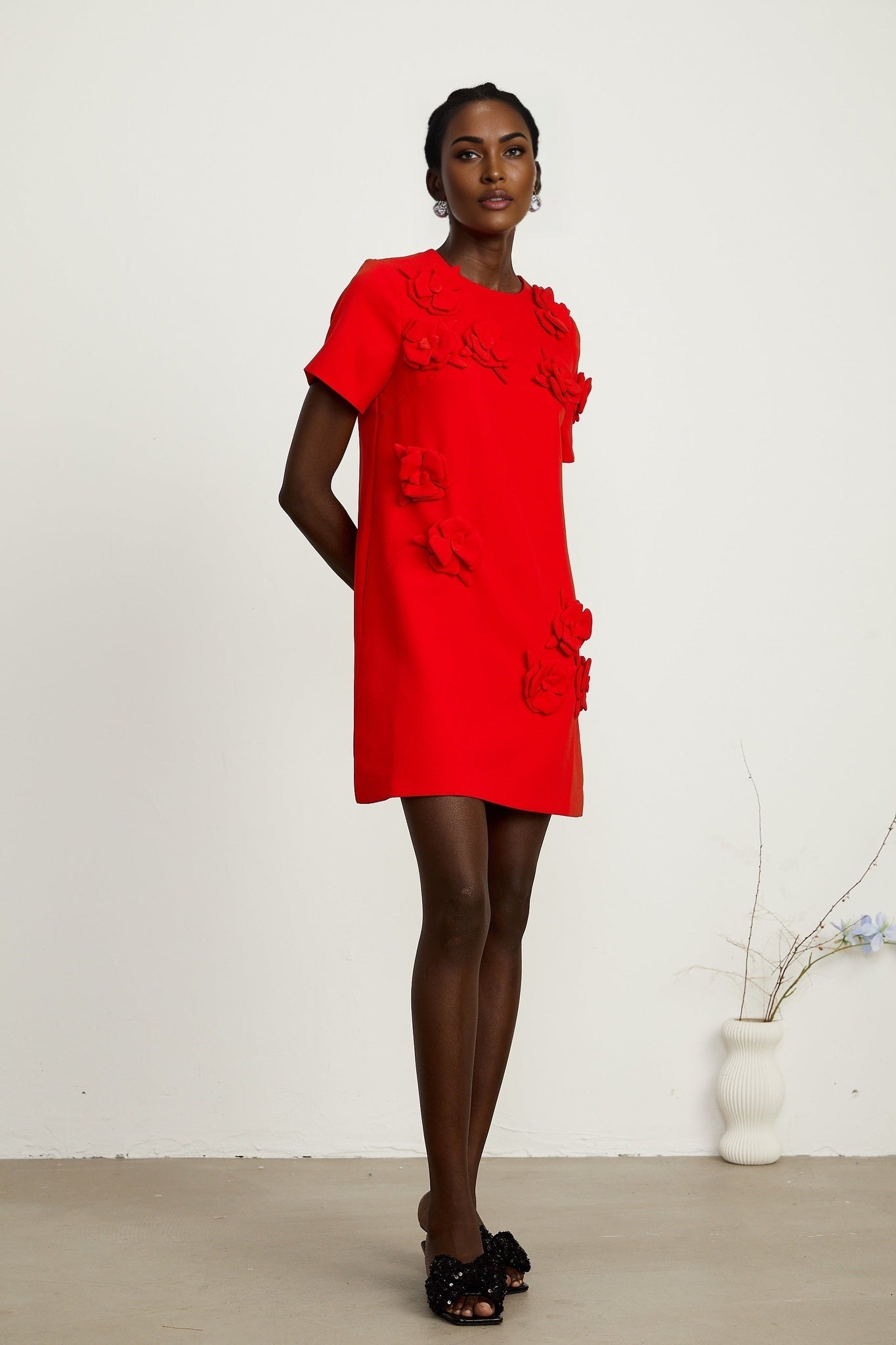 A red mini dress with short sleeves and floral details worn by a female model against a plain background